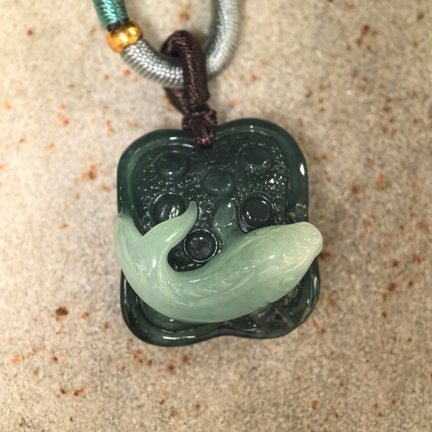 Close-up of light green fish carving over dark green jadeite lotus seed background.
