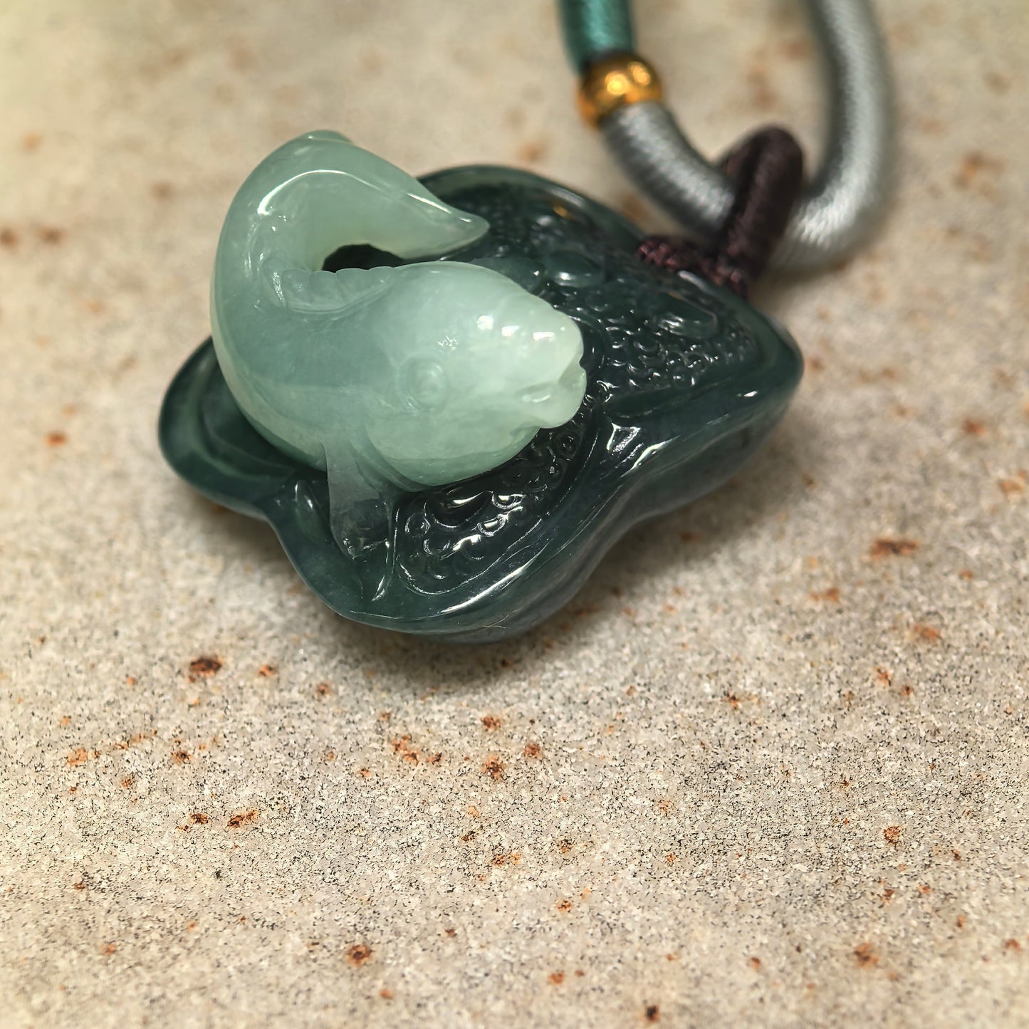 Side view of three-dimensional fish lotus jadeite pendant showing rounded carved details.
