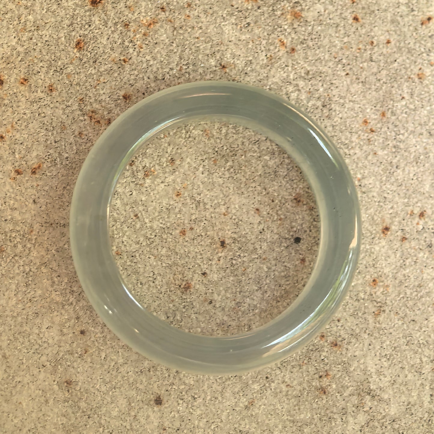 Top view of slim light green jadeite ring band on stone surface, showing circular shape and translucent icy texture.
