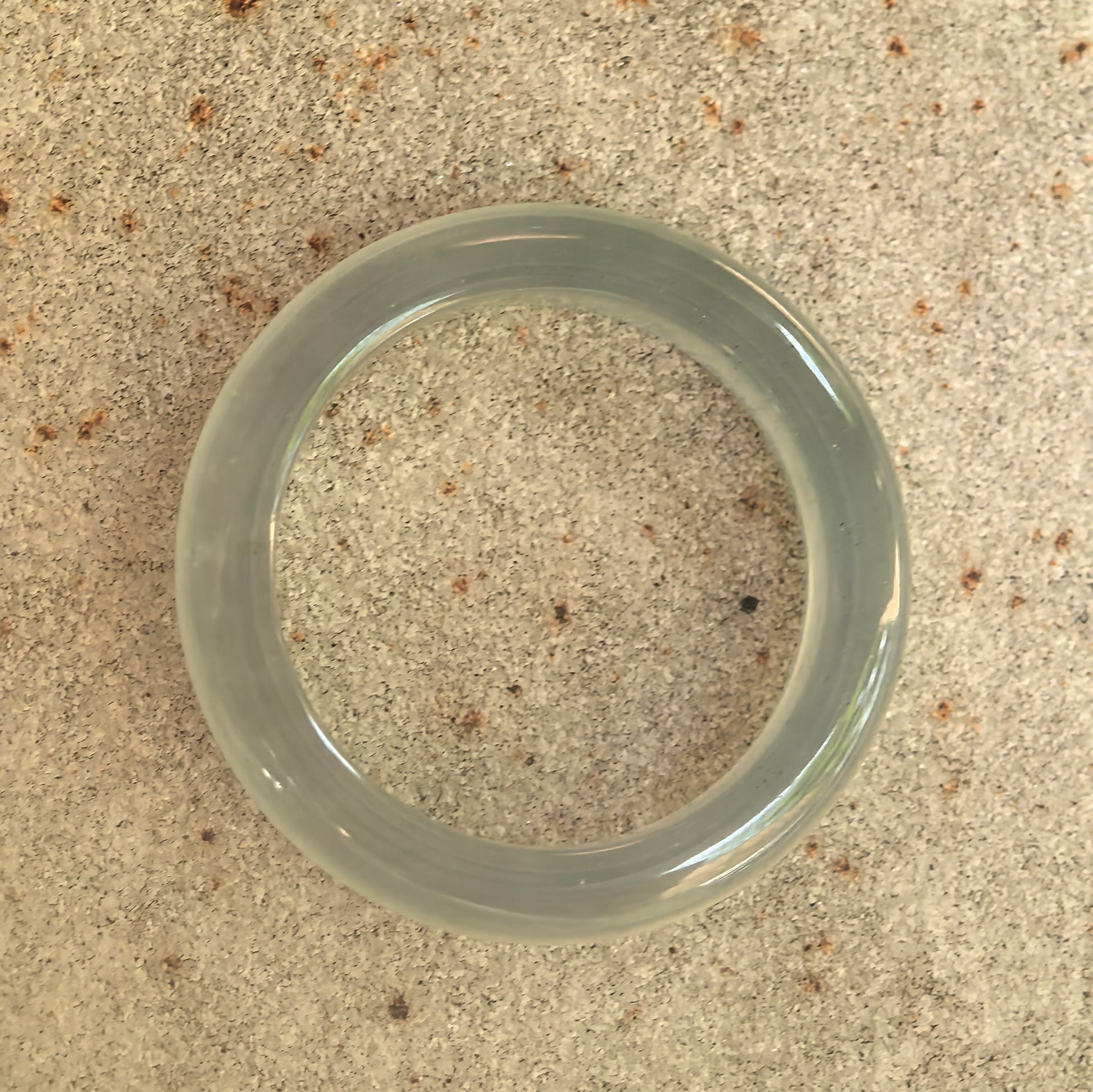 Top view of slim light green jadeite ring band on stone surface, showing circular shape and translucent icy texture.

