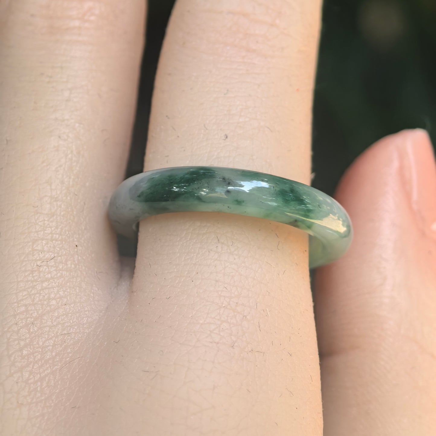 Close-up of green jadeite ring band showing darker green floating flower pattern and smooth polished luster.
