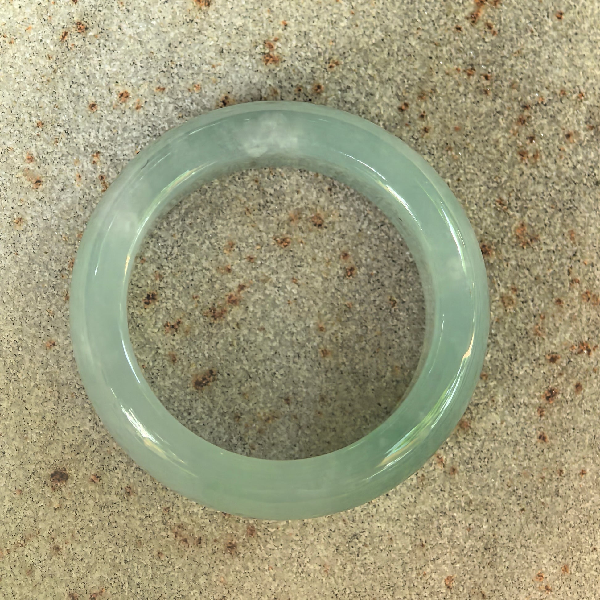 Top view of light green Burmese jadeite ring band on stone surface, showing circular band shape and smooth polish.
