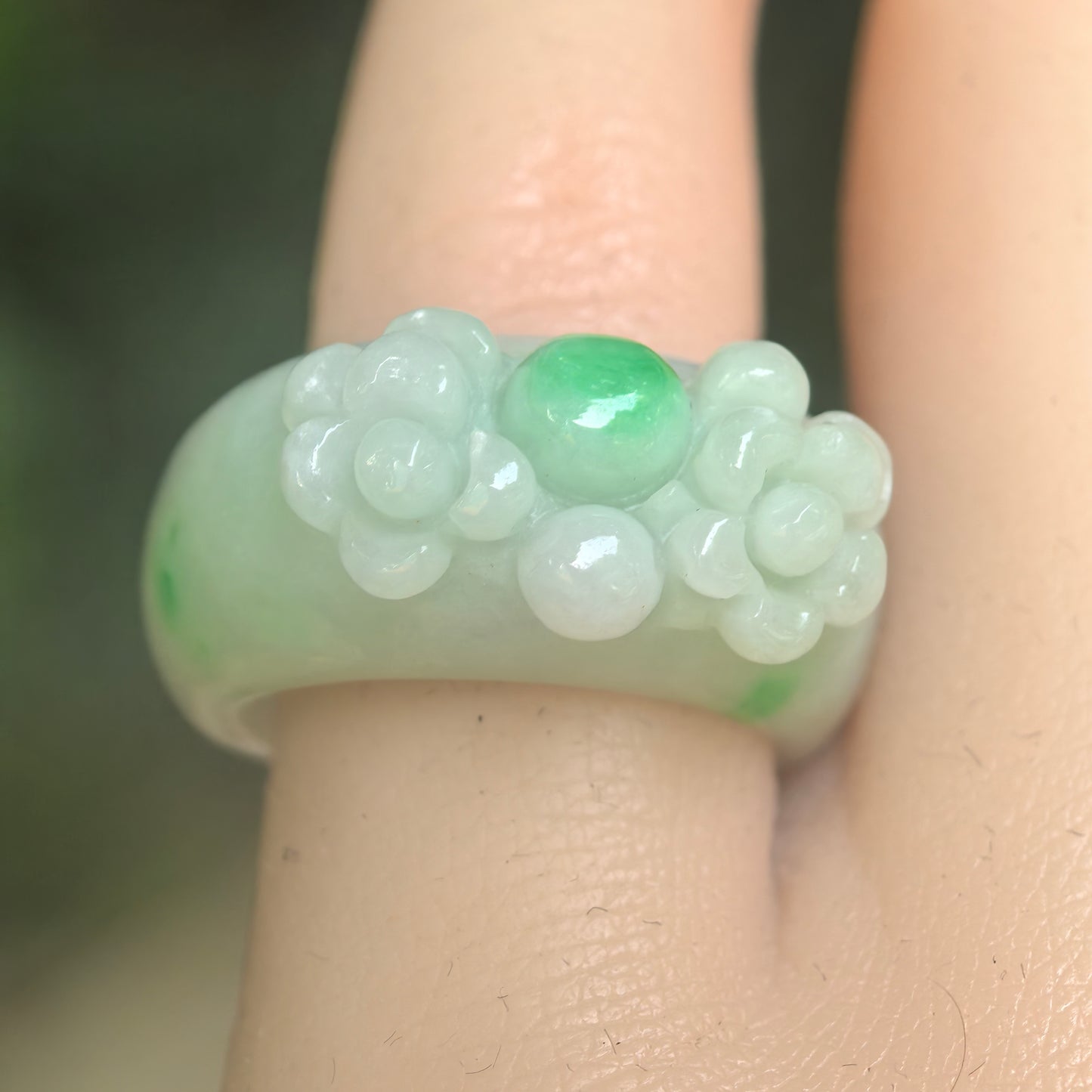 Close-up of light green jadeite ring band showing raised flower carving and smooth polished luster.
