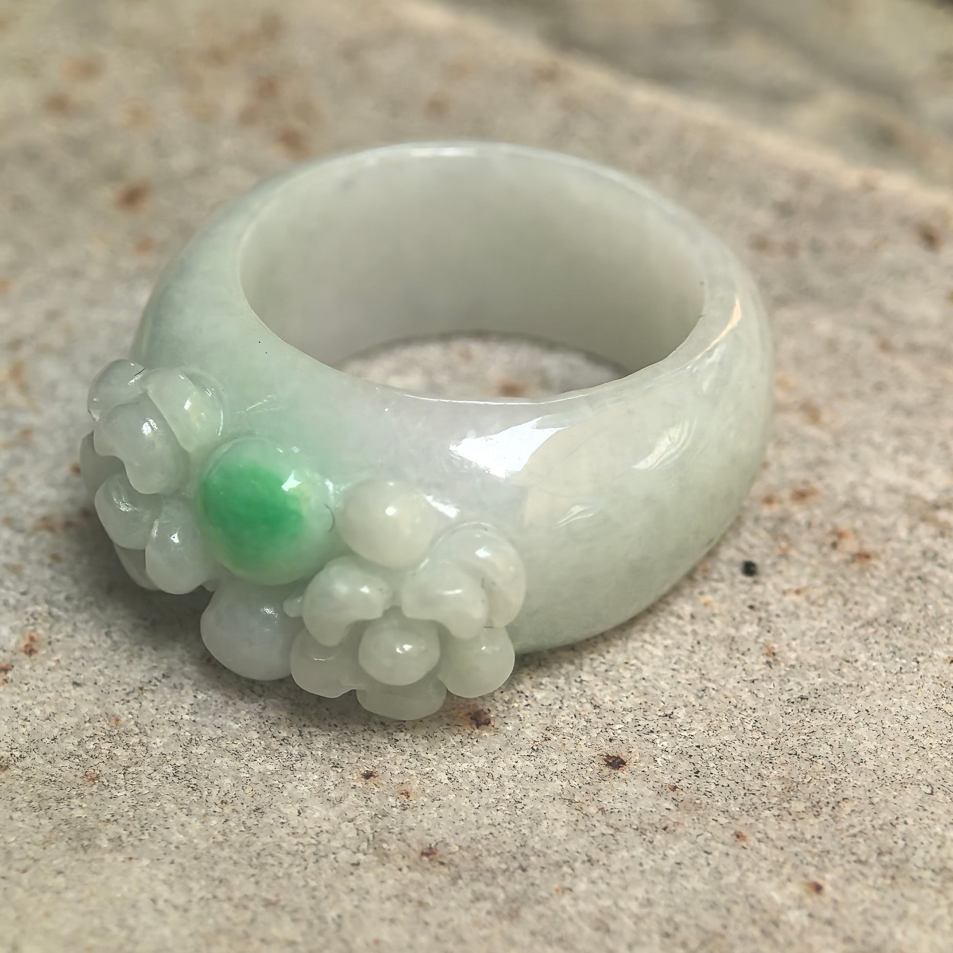 Side view of glutinous jadeite ring band showing rounded structure and carved flower detail.
