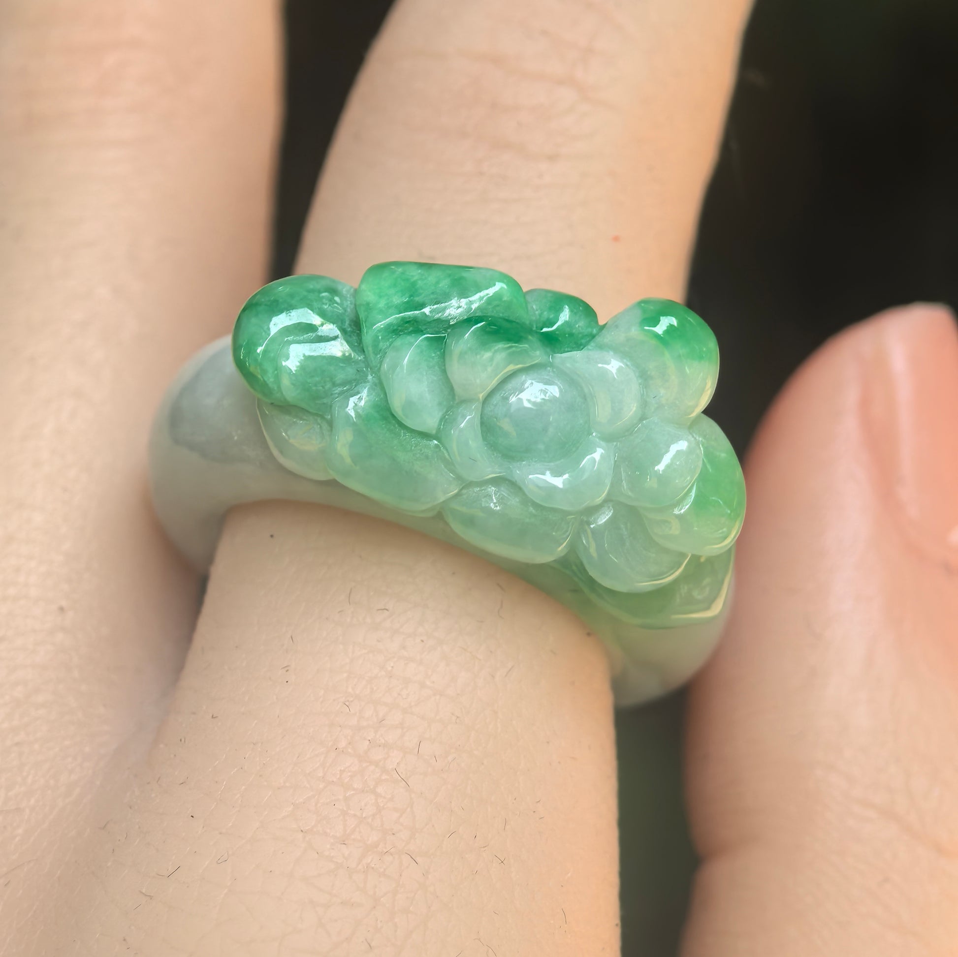 Close-up of green floral carved jadeite ring band showing raised flower petals and smooth luster.
