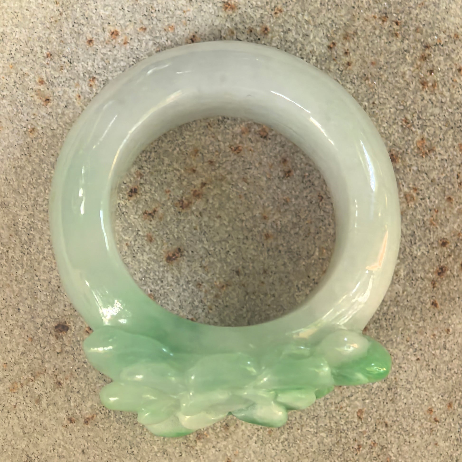 Top view of light green jadeite ring band with brighter green flower carving on the front.

