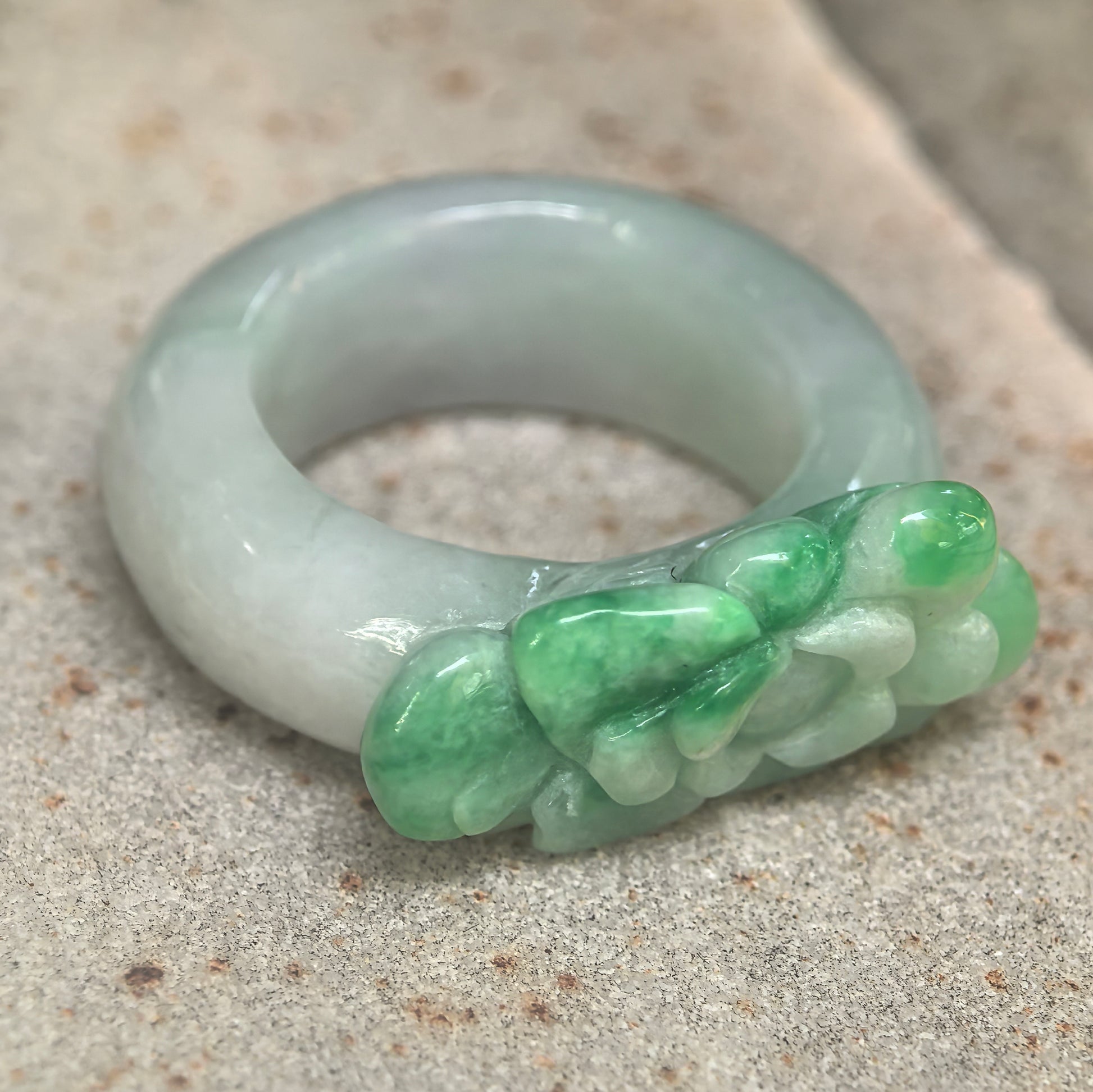 Side view of carved jadeite ring band showing thick rounded profile and sculptural floral design.
