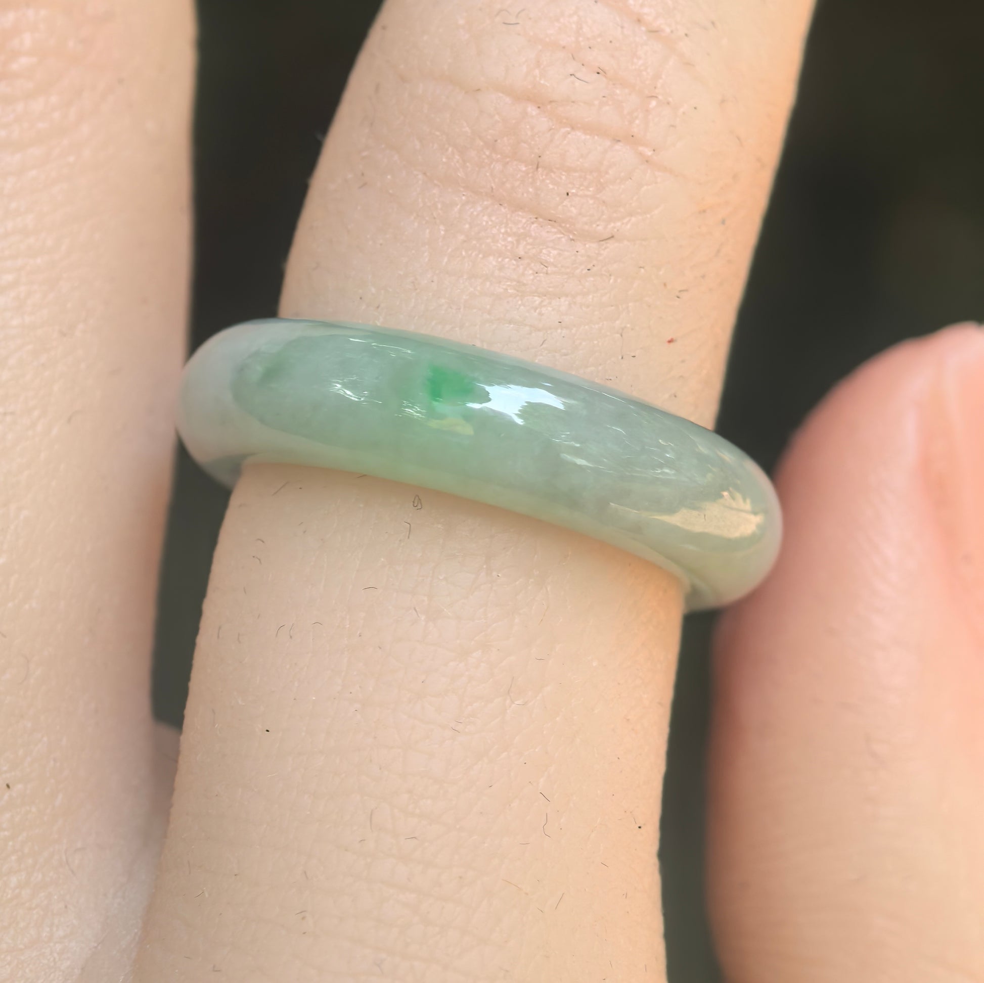 Close-up of pale green jadeite ring band showing smooth luster and small green accent.
