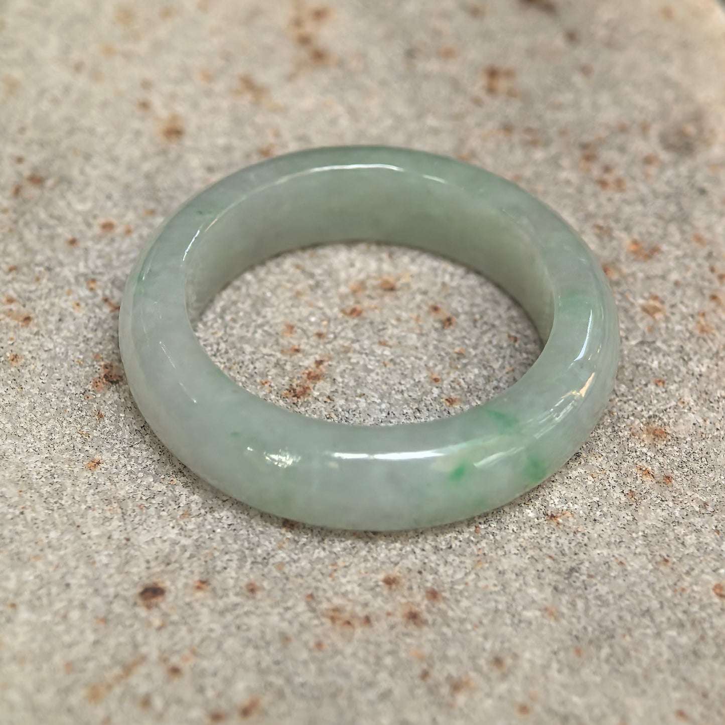 Side view of natural light green jadeite ring band showing medium-width polished form.
