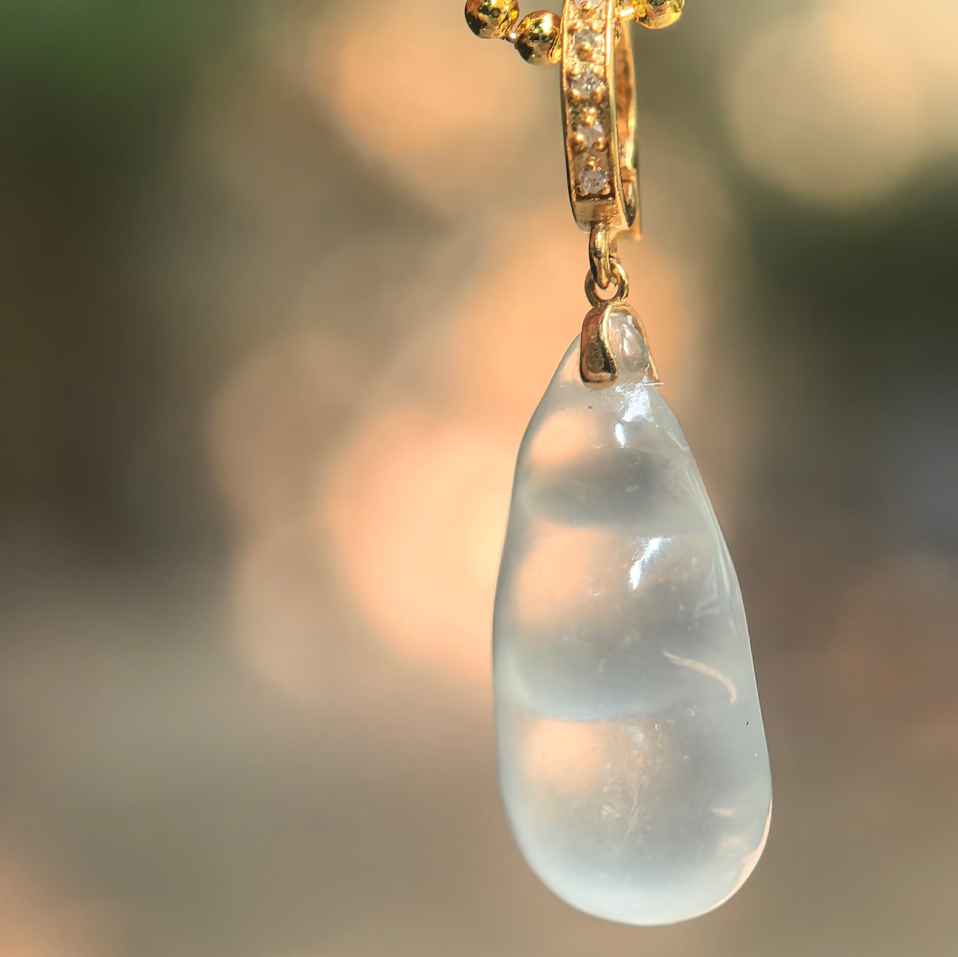 Natural Grade-A icy translucent white bean jadeite pendant with 18K gold hanging under light.

