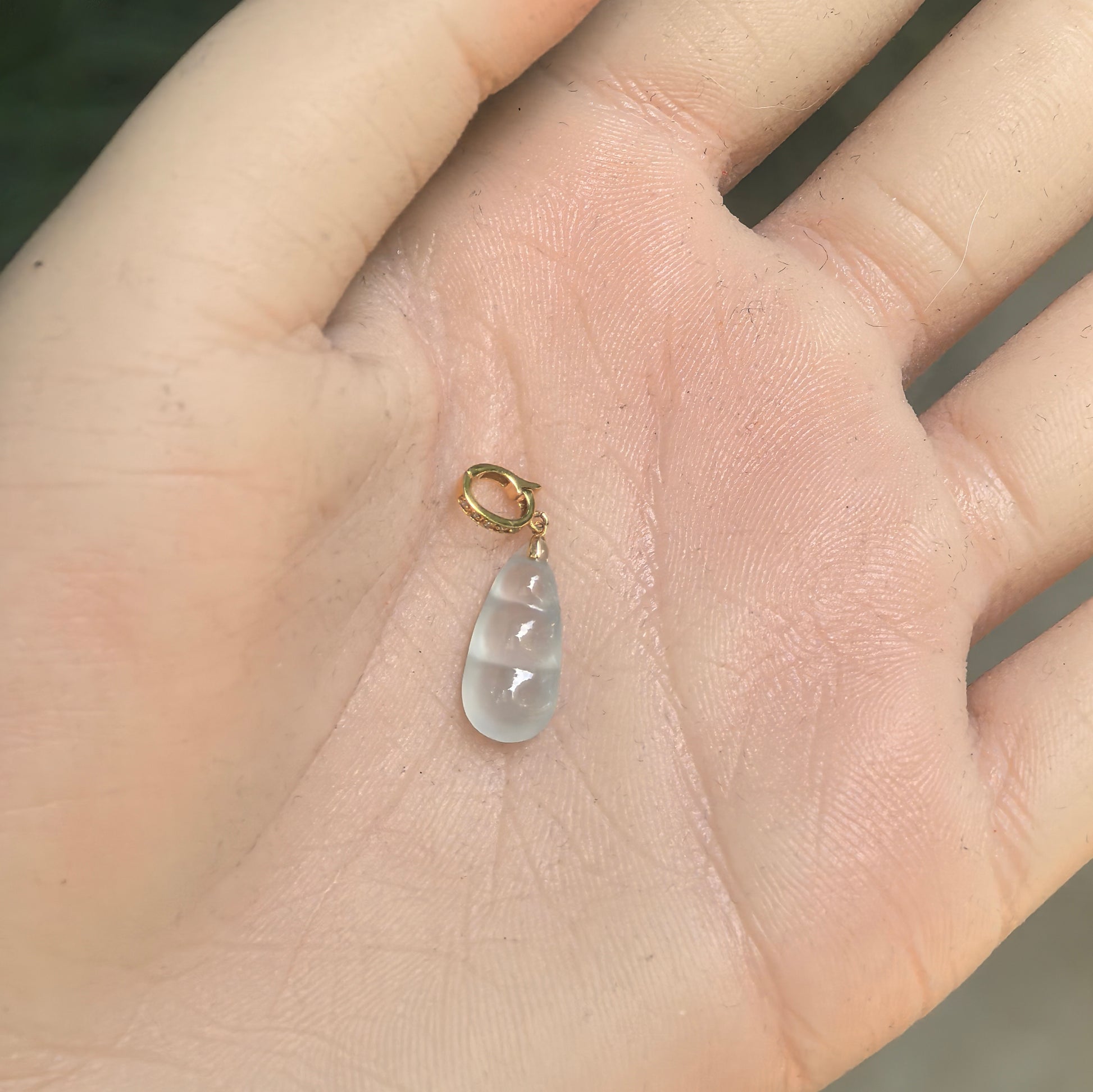 Small white jadeite bean pendant with smooth double-sided rounded carving shown on hand.

