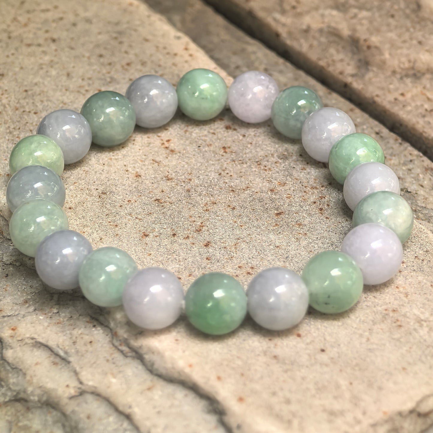 Glutinous light spring jadeite beaded bracelet arranged in a full circle on stone surface.
