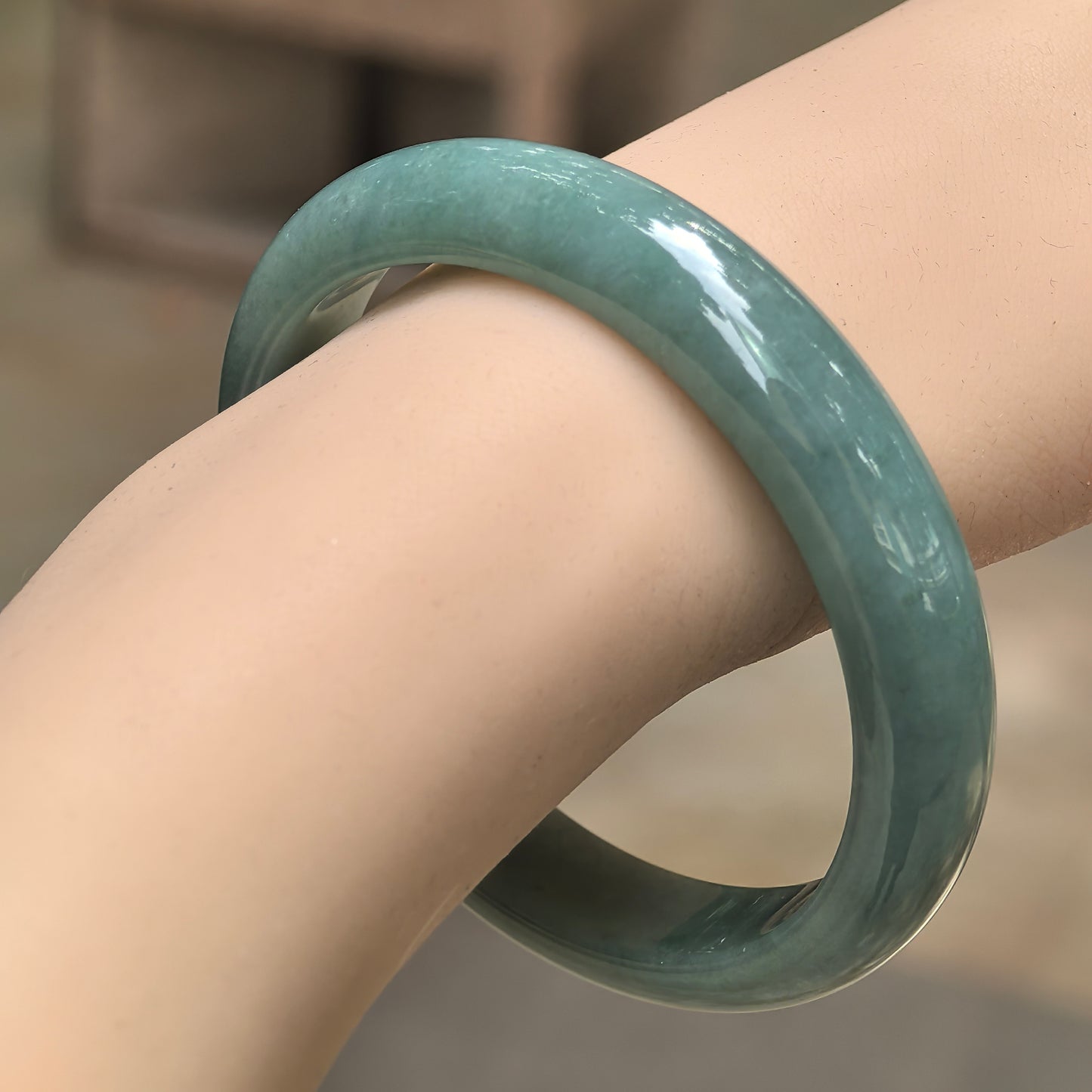Natural Grade-A glutinous oil-green D-shape jadeite bangle worn on wrist under natural light.
