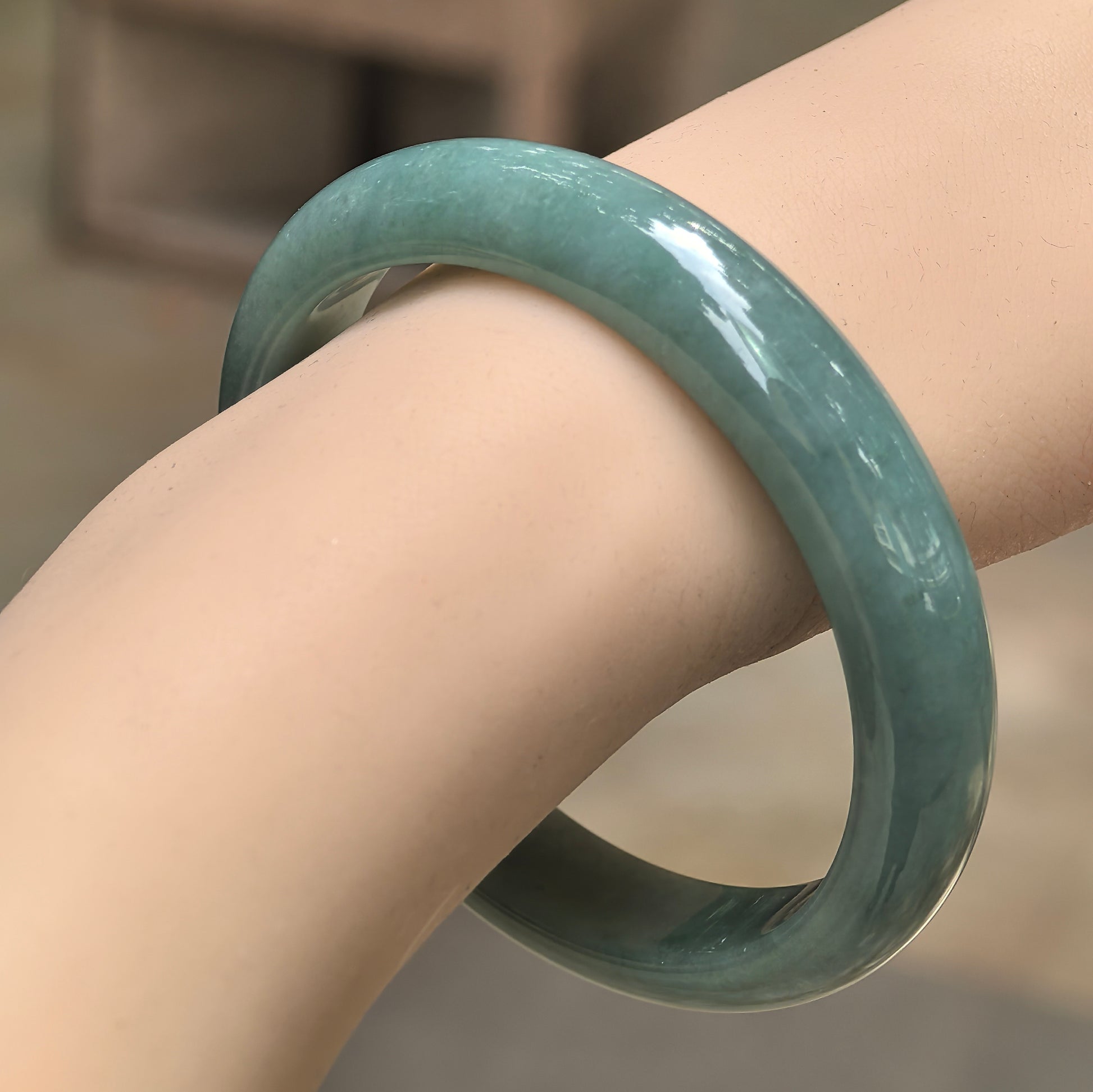 Natural Grade-A glutinous oil-green D-shape jadeite bangle worn on wrist under natural light.
