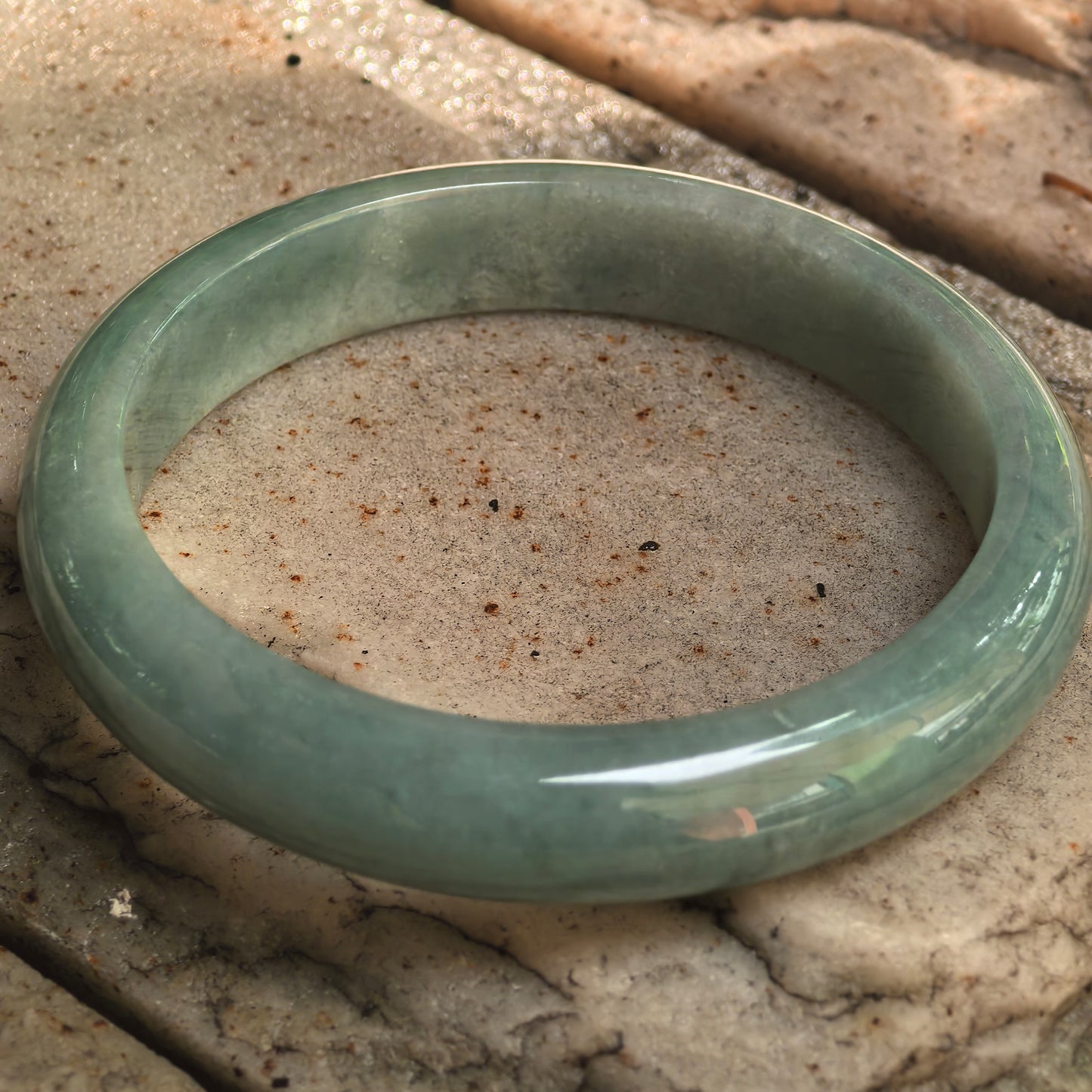 Natural Grade-A oil-green jadeite bangle displayed on stone surface with visible glutinous texture.
