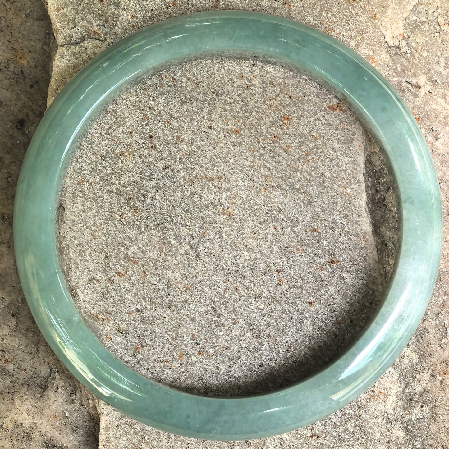 Top view of D-shape jadeite bangle showing full round form and calm green color.
