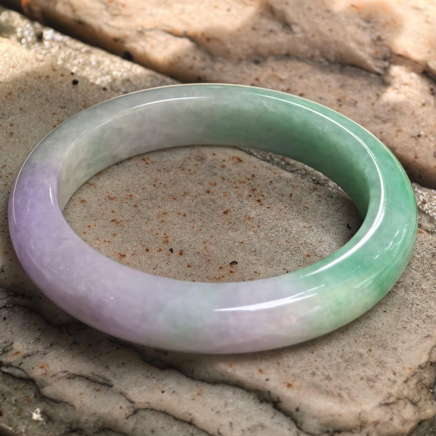 Natural jadeite bangle displayed on stone surface with green and lavender color transition.

