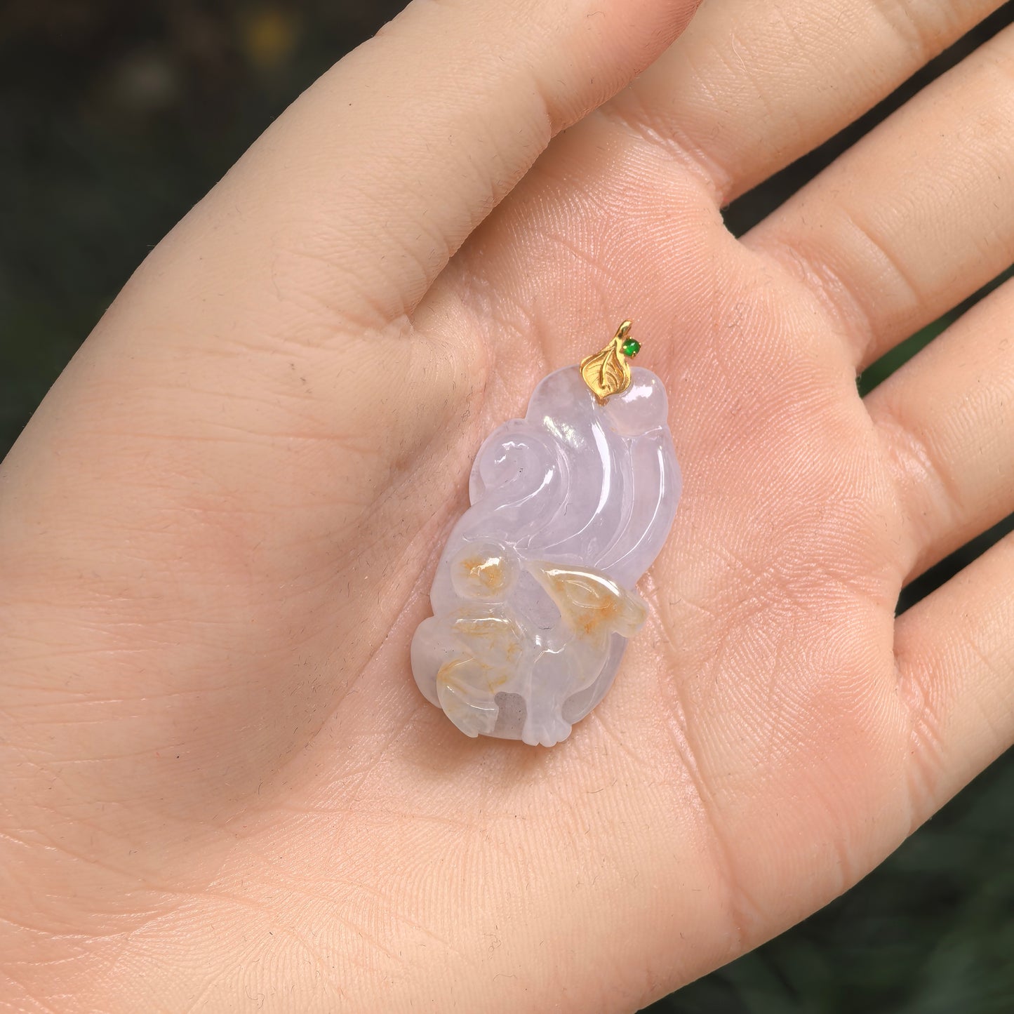 Pale lavender-white jadeite fox pendant with brownish yellow skin accents shown in hand.
