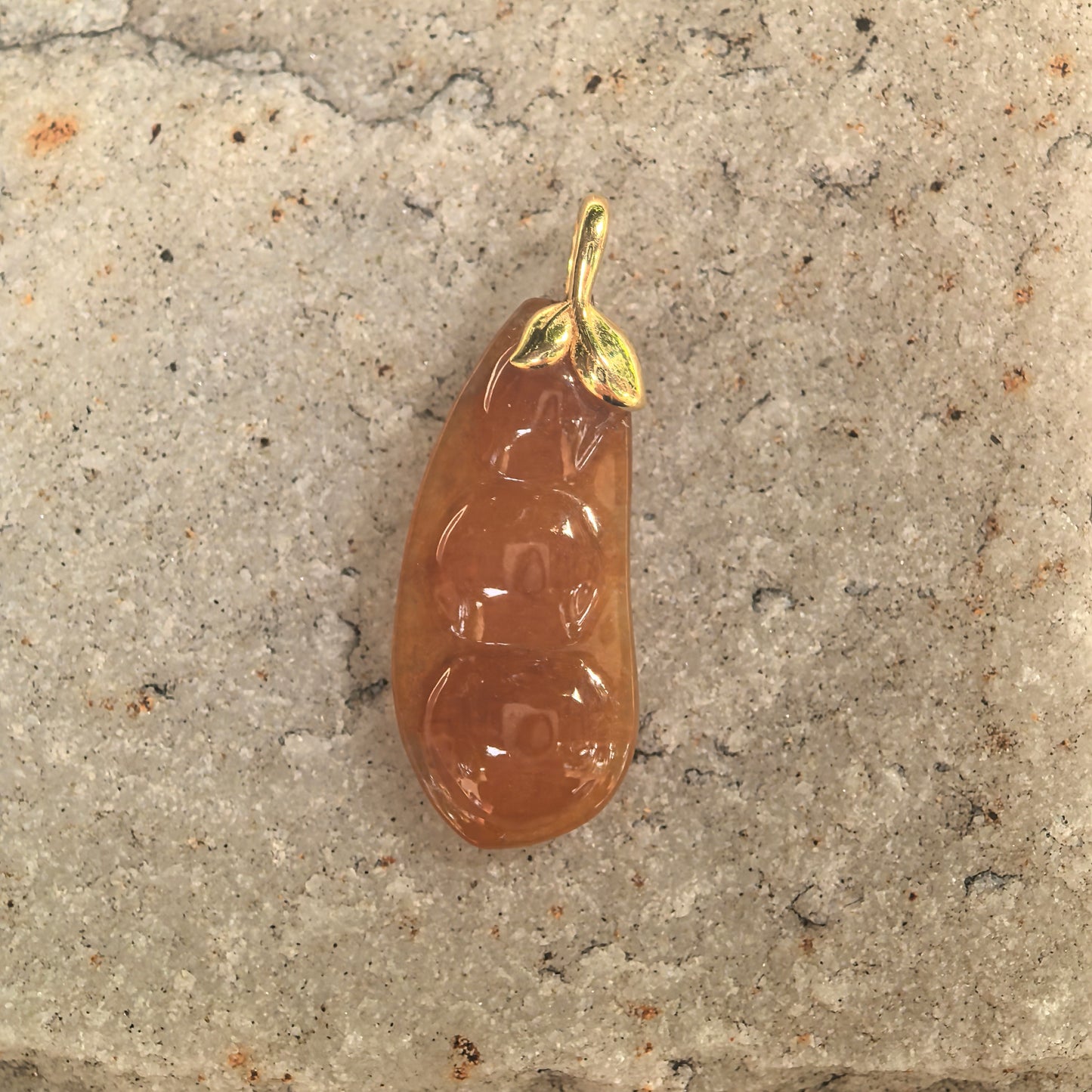 Close-up of icy glutinous orange-red jadeite bean pendant showing raised bean carving.
