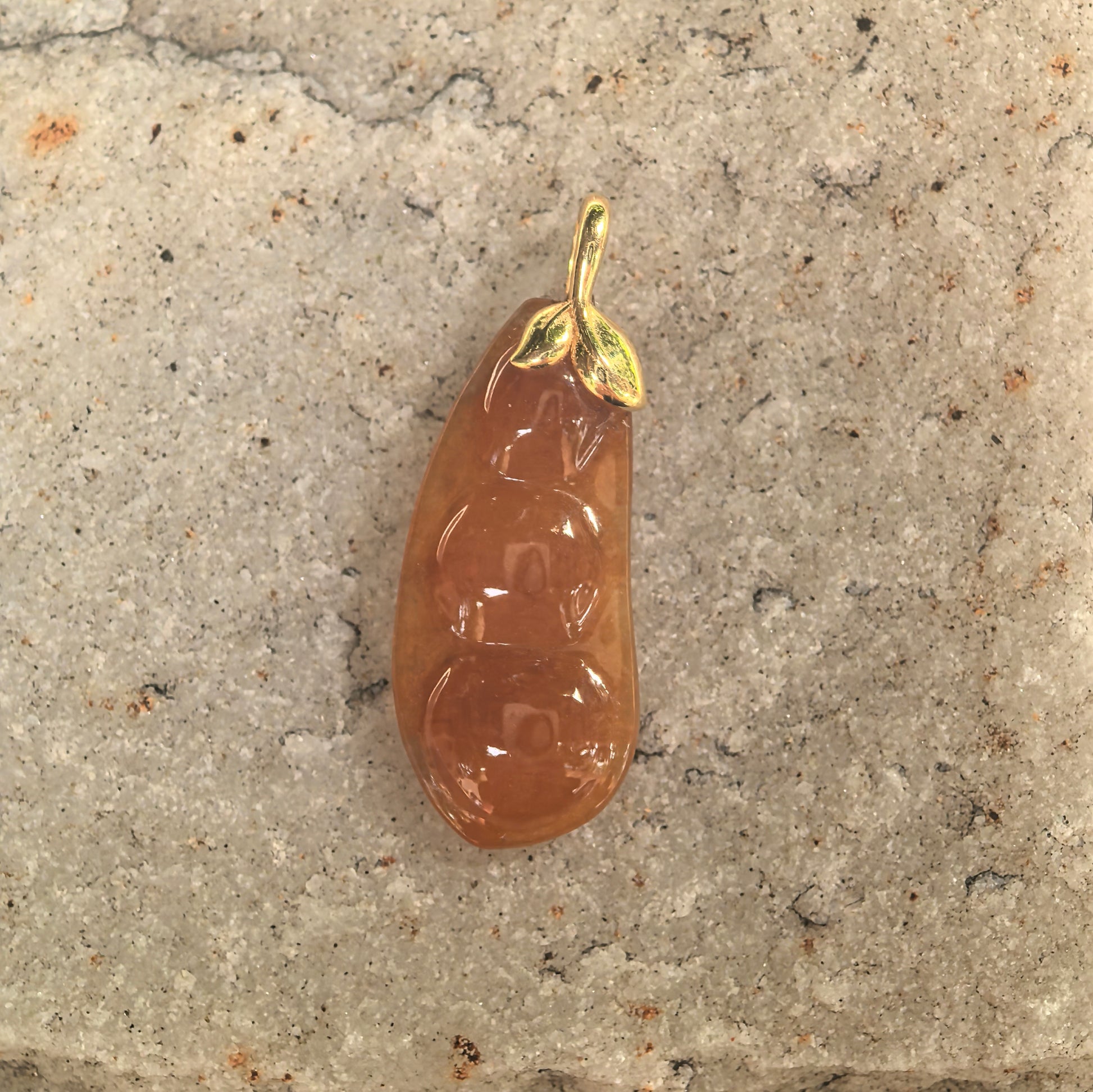 Close-up of icy glutinous orange-red jadeite bean pendant showing raised bean carving.
