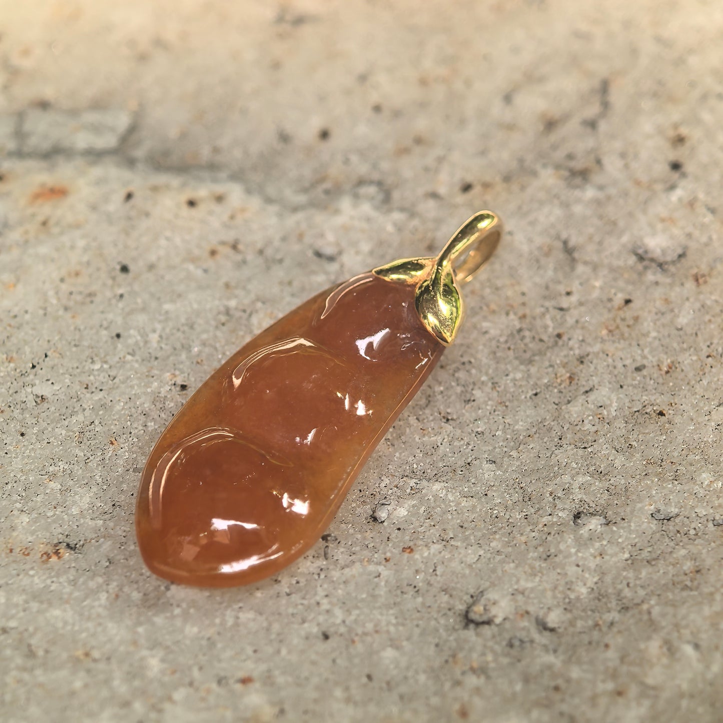 Natural Grade-A brownish yellow orange jadeite pendant displayed on stone surface.

