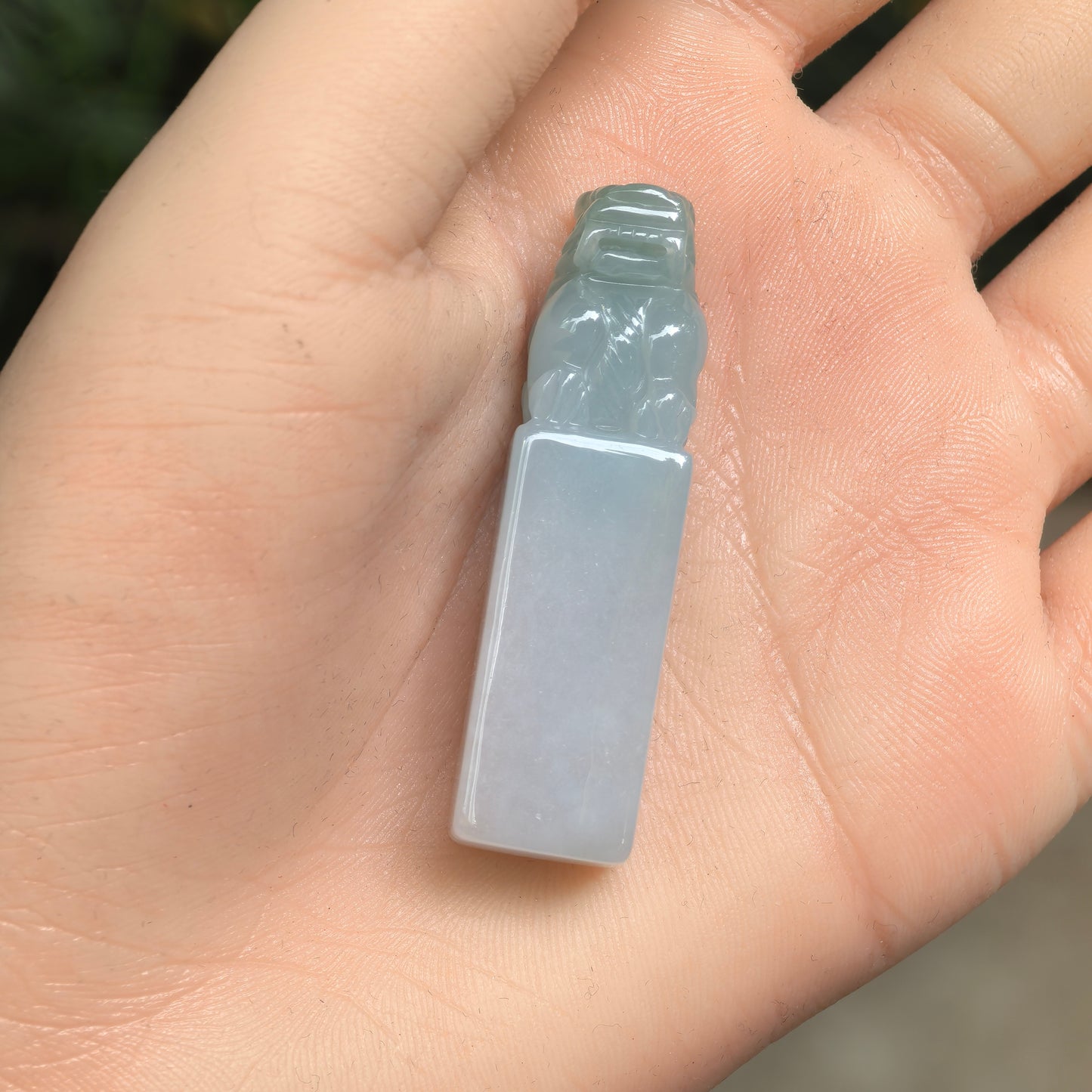 Natural Grade-A icy glutinous light green jadeite lion seal ornament shown in hand.
