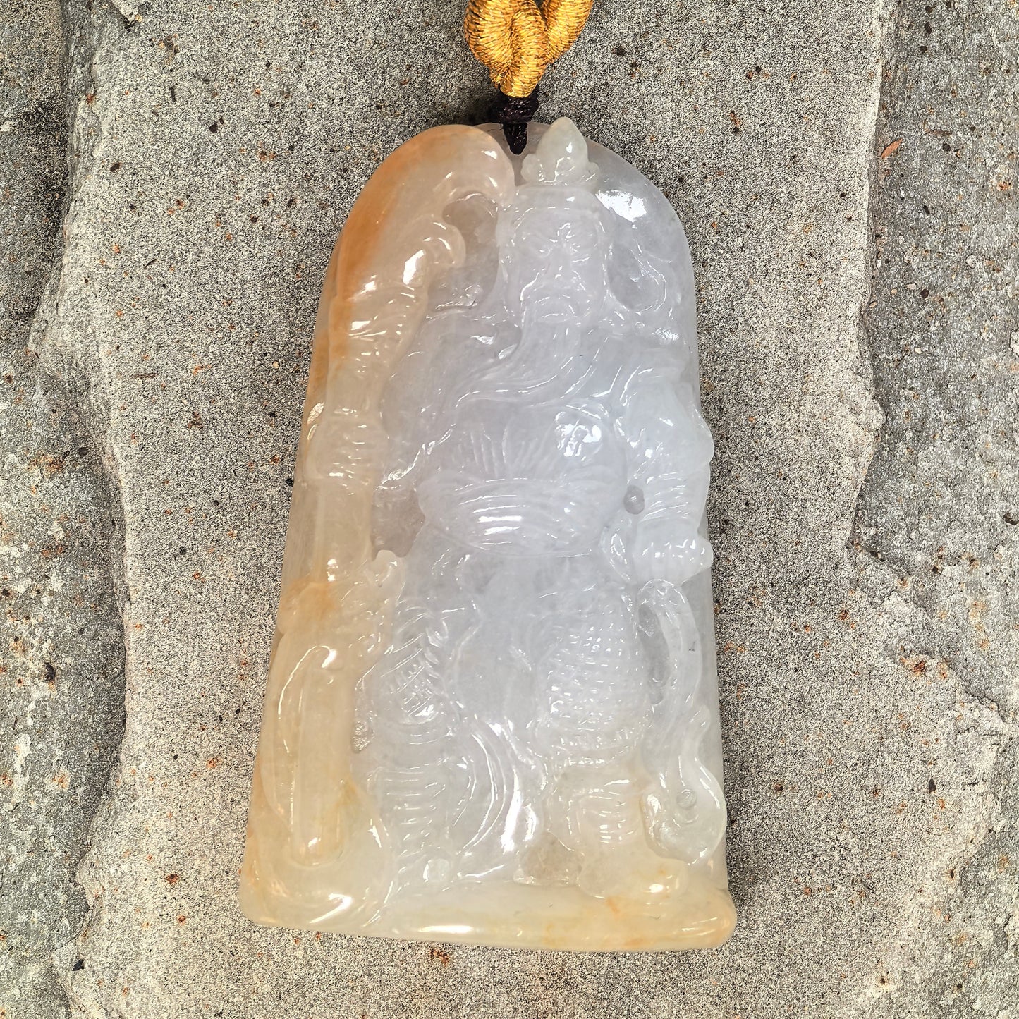 Close-up of white and yellow Burmese jadeite Guan Gong pendant showing detailed figure carving.
