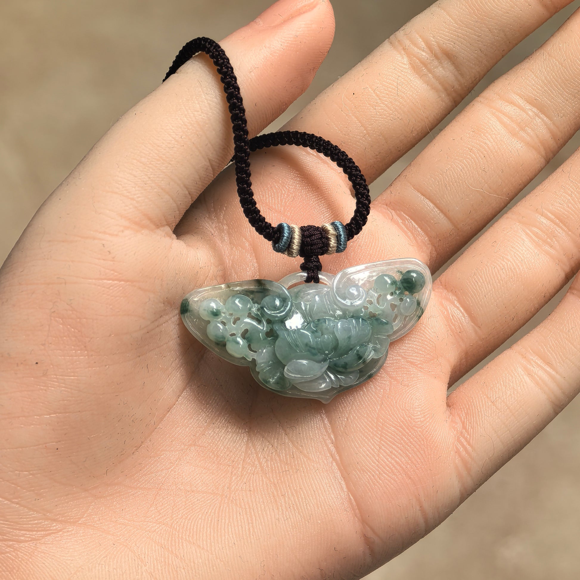 Green butterfly-shaped jadeite pendant with floral relief carving shown on hand.
