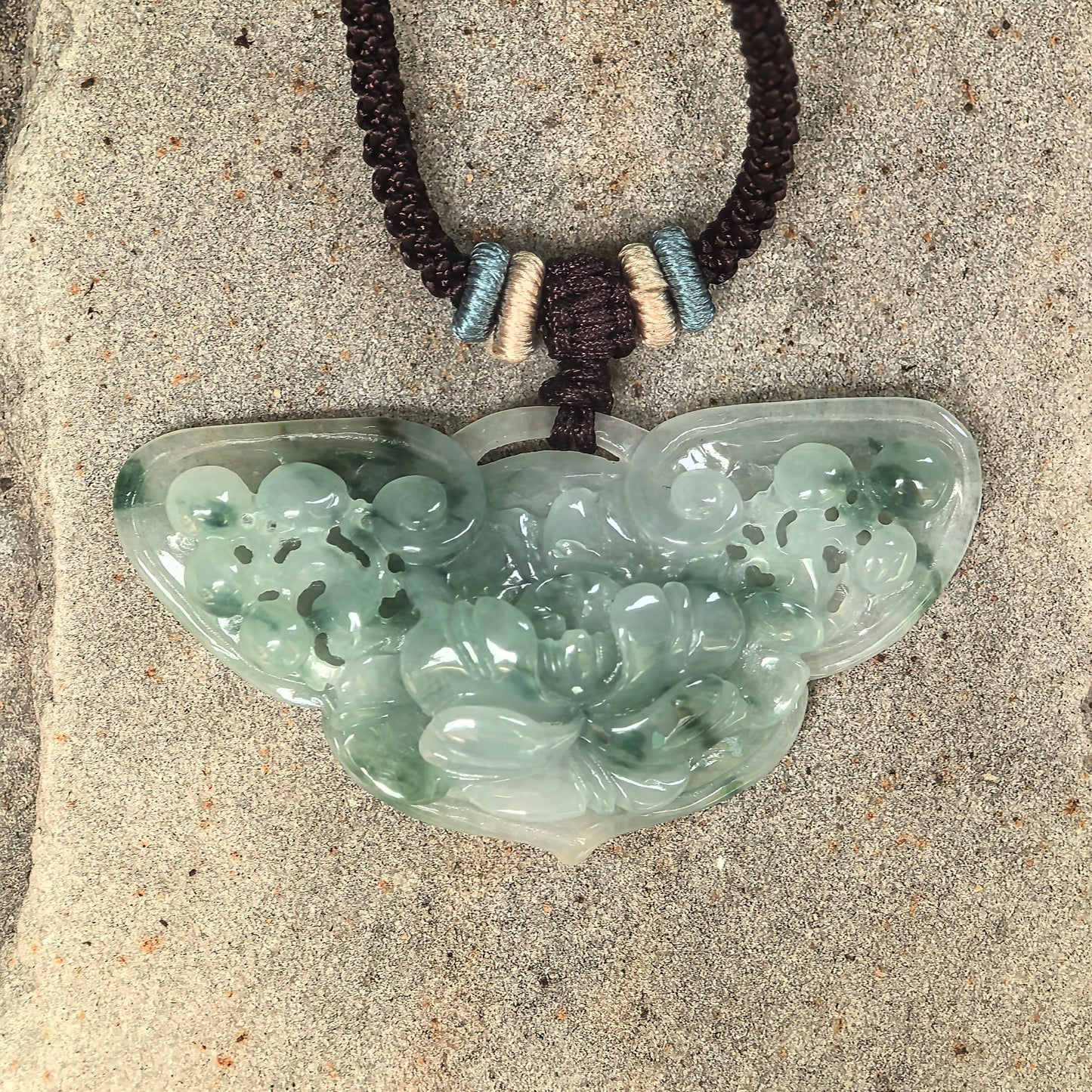 Close-up of glutinous green jadeite butterfly pendant showing carved flowers and openwork details.

