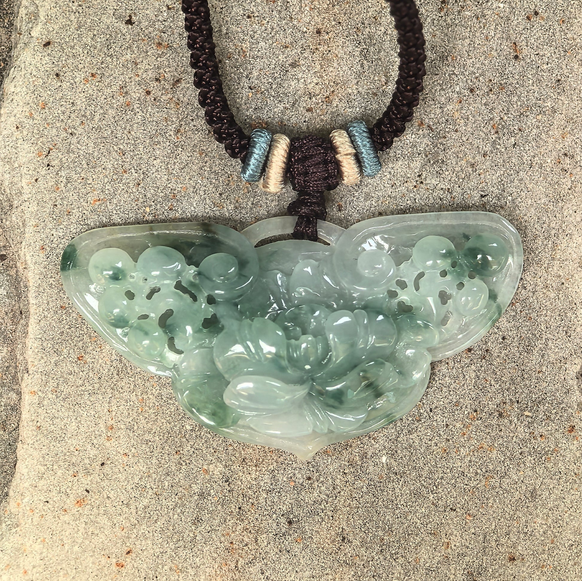 Close-up of glutinous green jadeite butterfly pendant showing carved flowers and openwork details.
