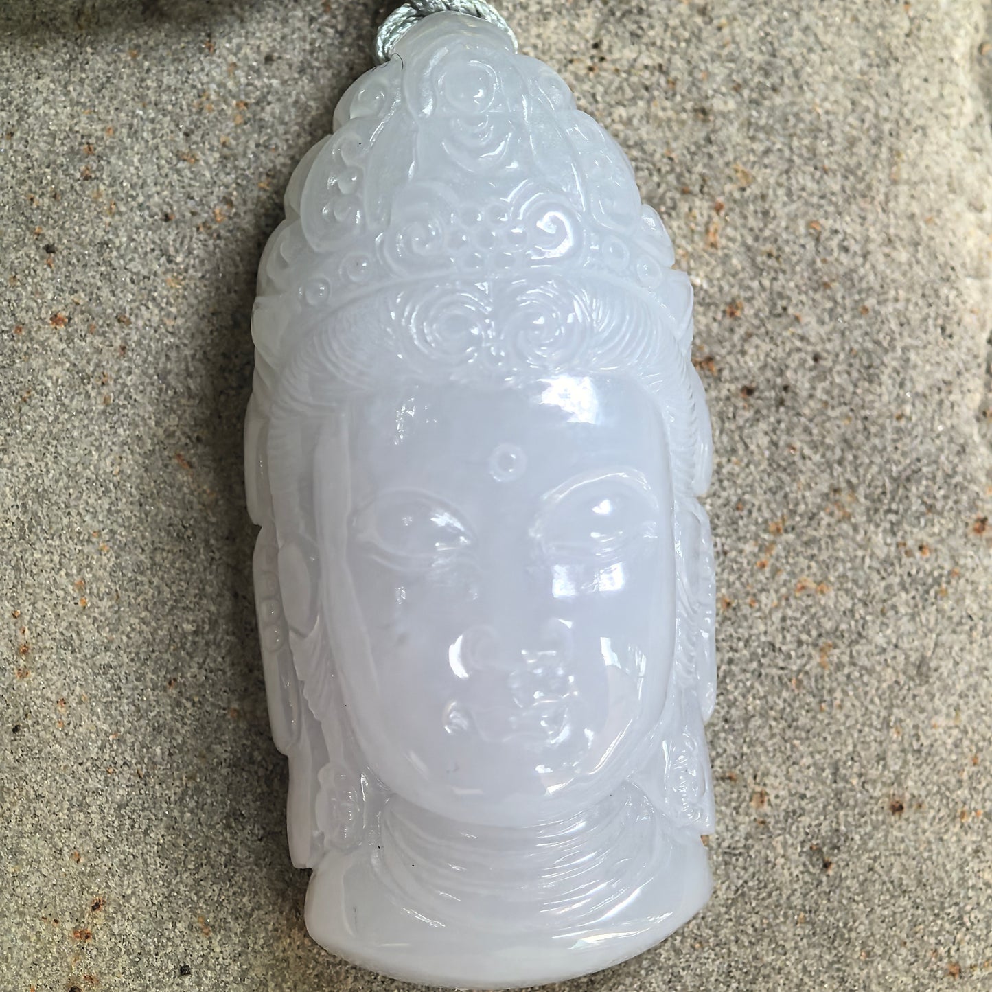 Close-up of glutinous jadeite Buddha head pendant showing detailed facial and crown carving.
