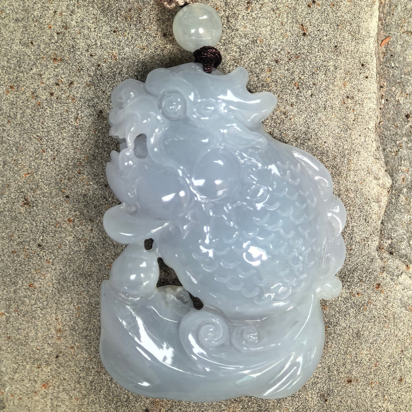 Close-up of glutinous jadeite dragon-fish pendant showing carved scales and dragon head details.
