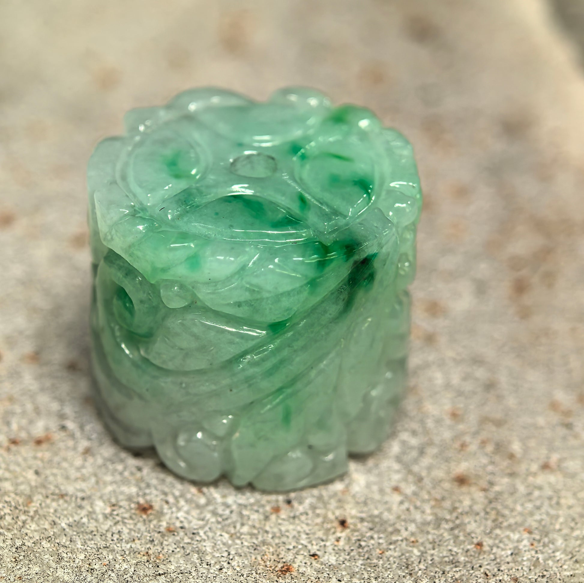 Close-up of green-white jadeite barrel bead showing raised floral carving and polished luster.
