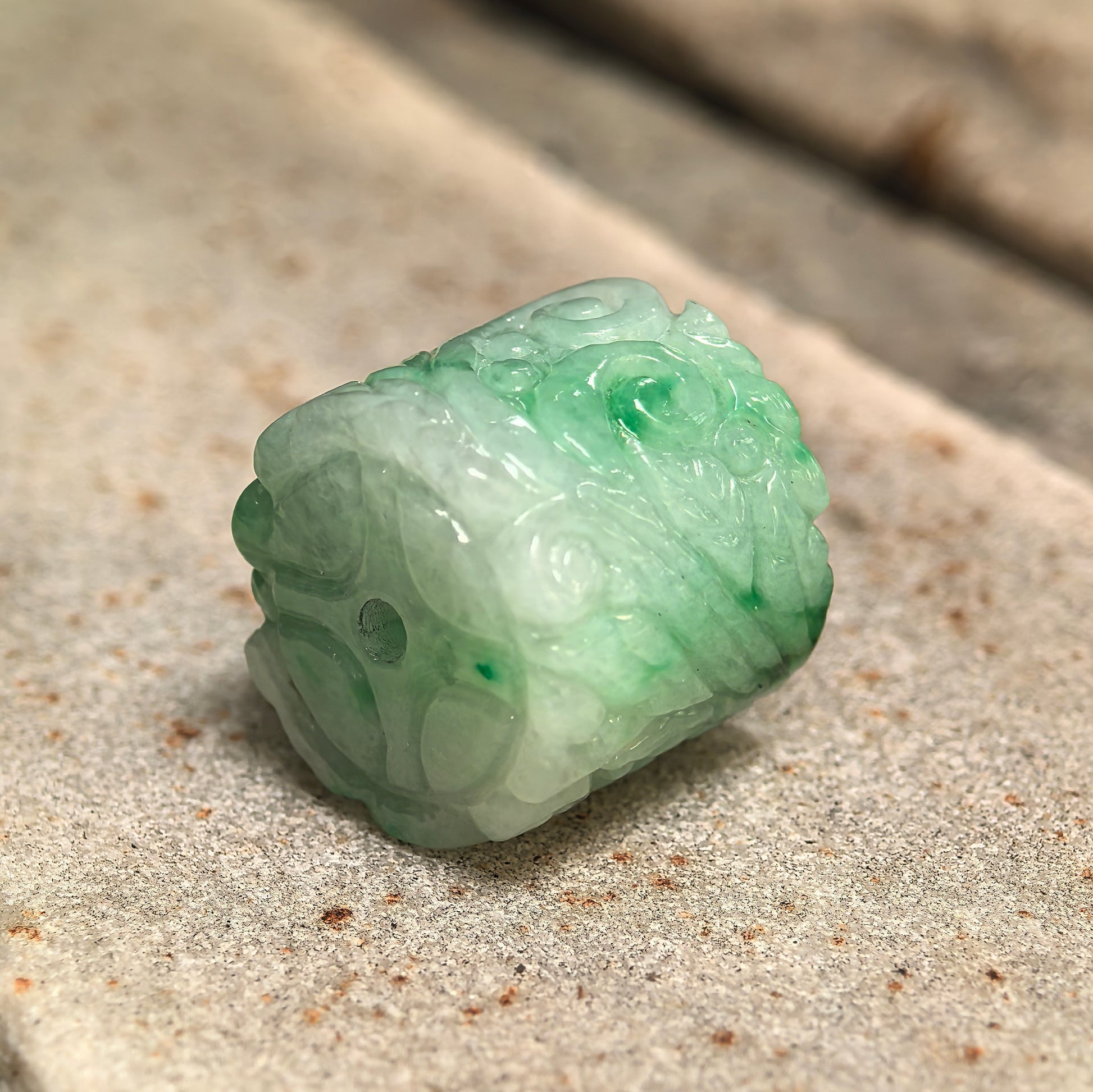 Side view of carved jadeite barrel bead pendant showing through-hole design and soft green color.
