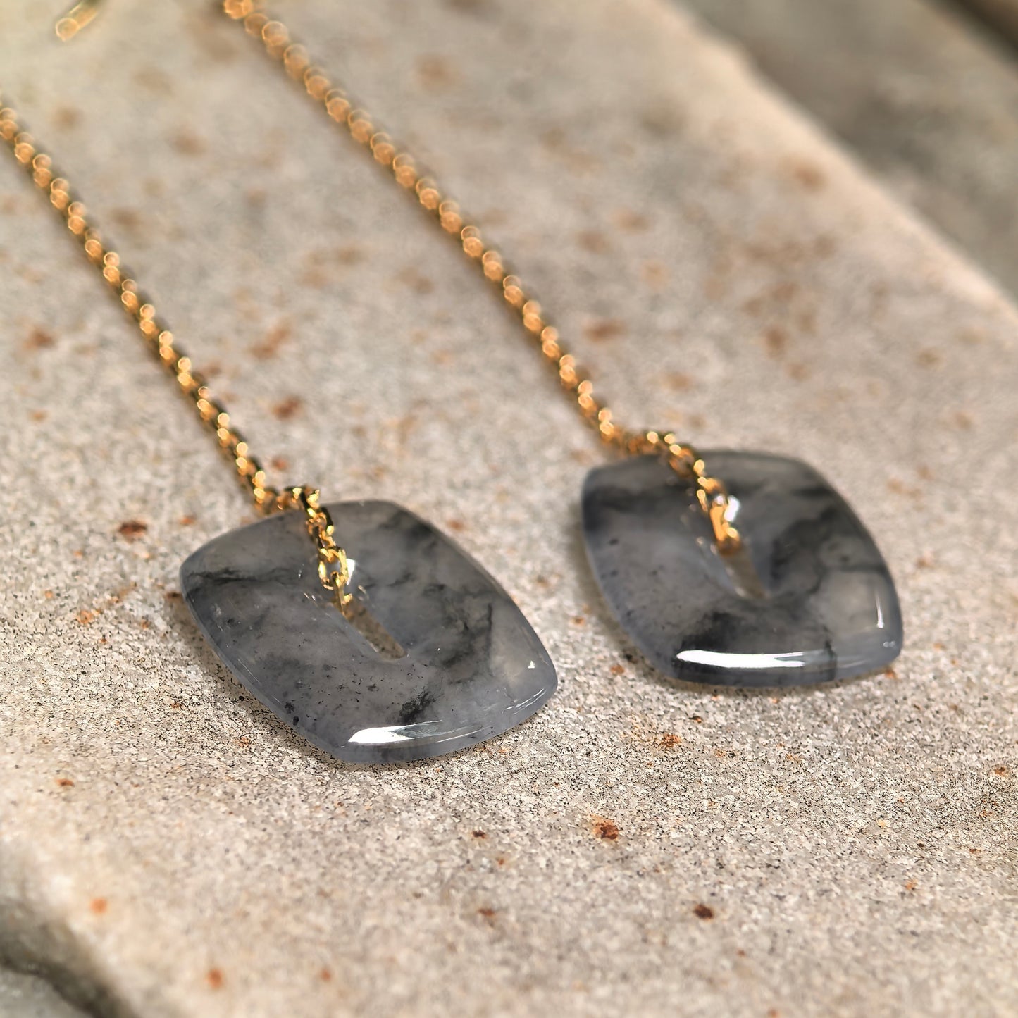 Close-up of icy black-gray jadeite earrings showing natural ink-like patterns and polished surface.

