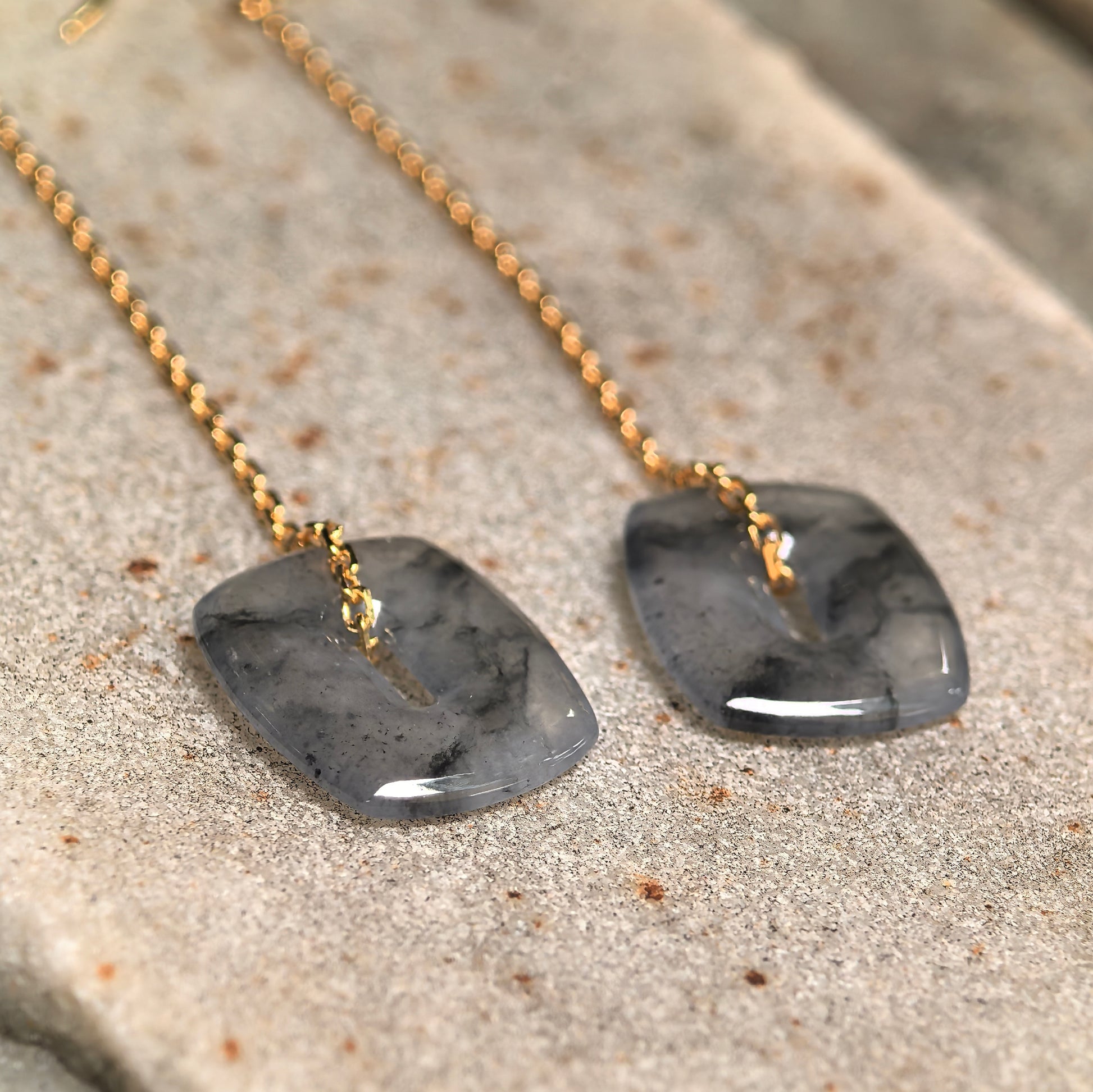 Close-up of icy black-gray jadeite earrings showing natural ink-like patterns and polished surface.
