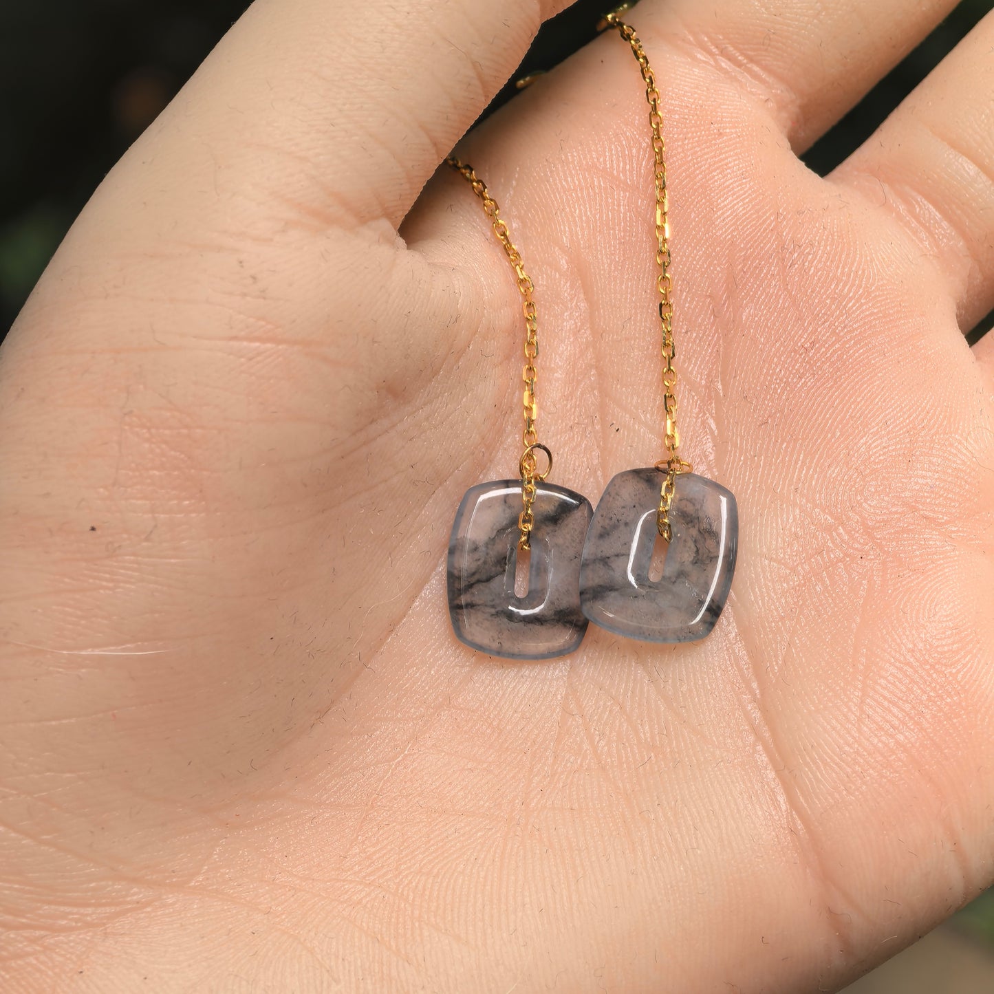 Natural untreated Burmese jadeite 18K gold earrings shown on hand with elegant long chain design.
