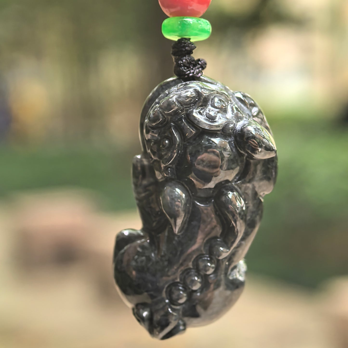 Natural Grade-A black chicken Pixiu jadeite pendant hanging in natural light, showing the three-dimensional carving and dark marbled tone.