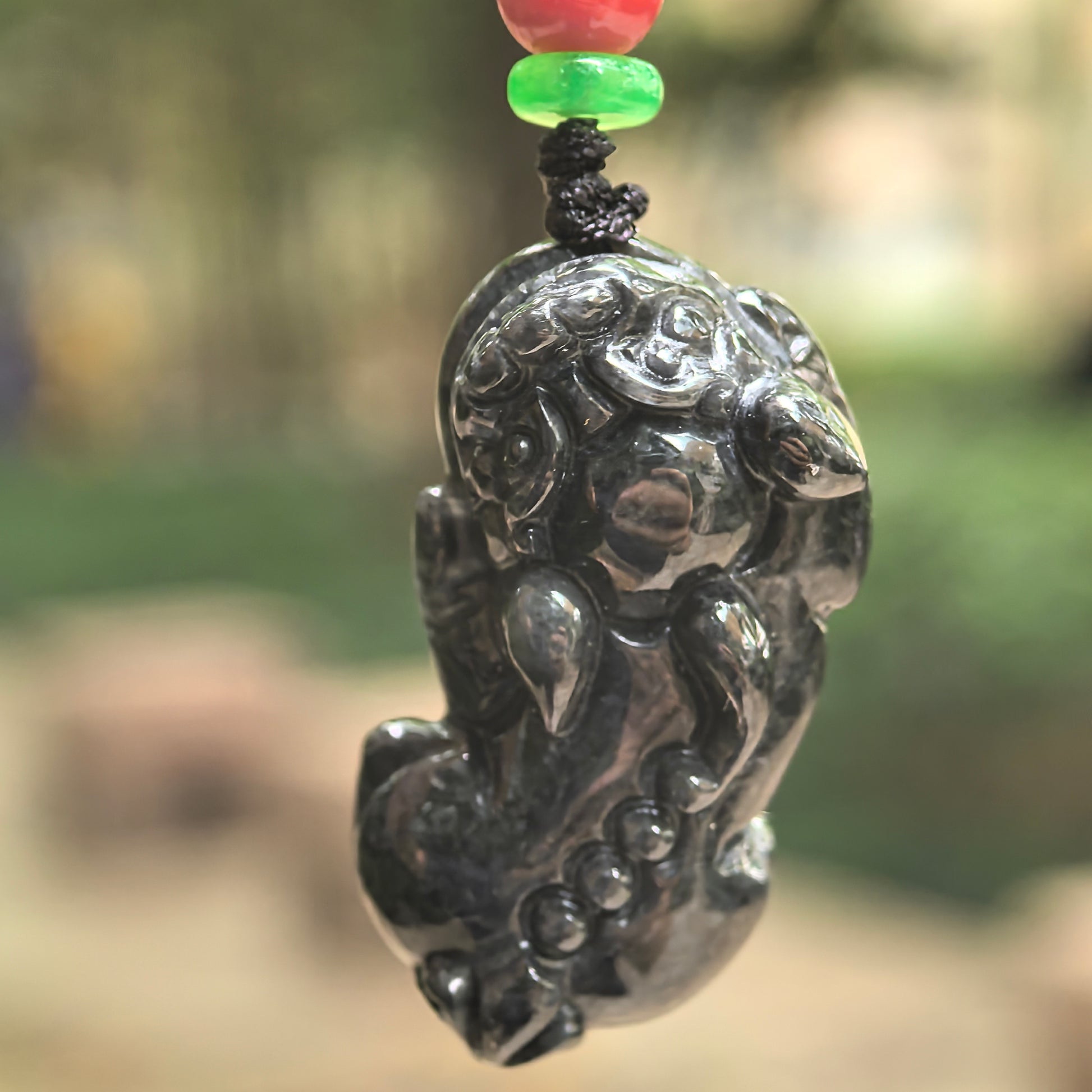 Natural Grade-A black chicken Pixiu jadeite pendant hanging in natural light, showing the three-dimensional carving and dark marbled tone.