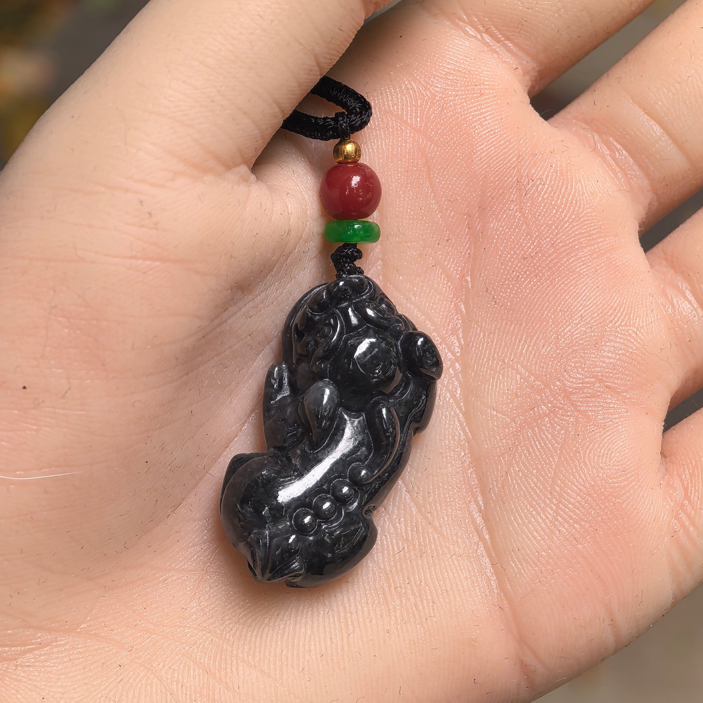 Black chicken Pixiu jadeite pendant shown in hand for size reference, highlighting its thick and compact form.