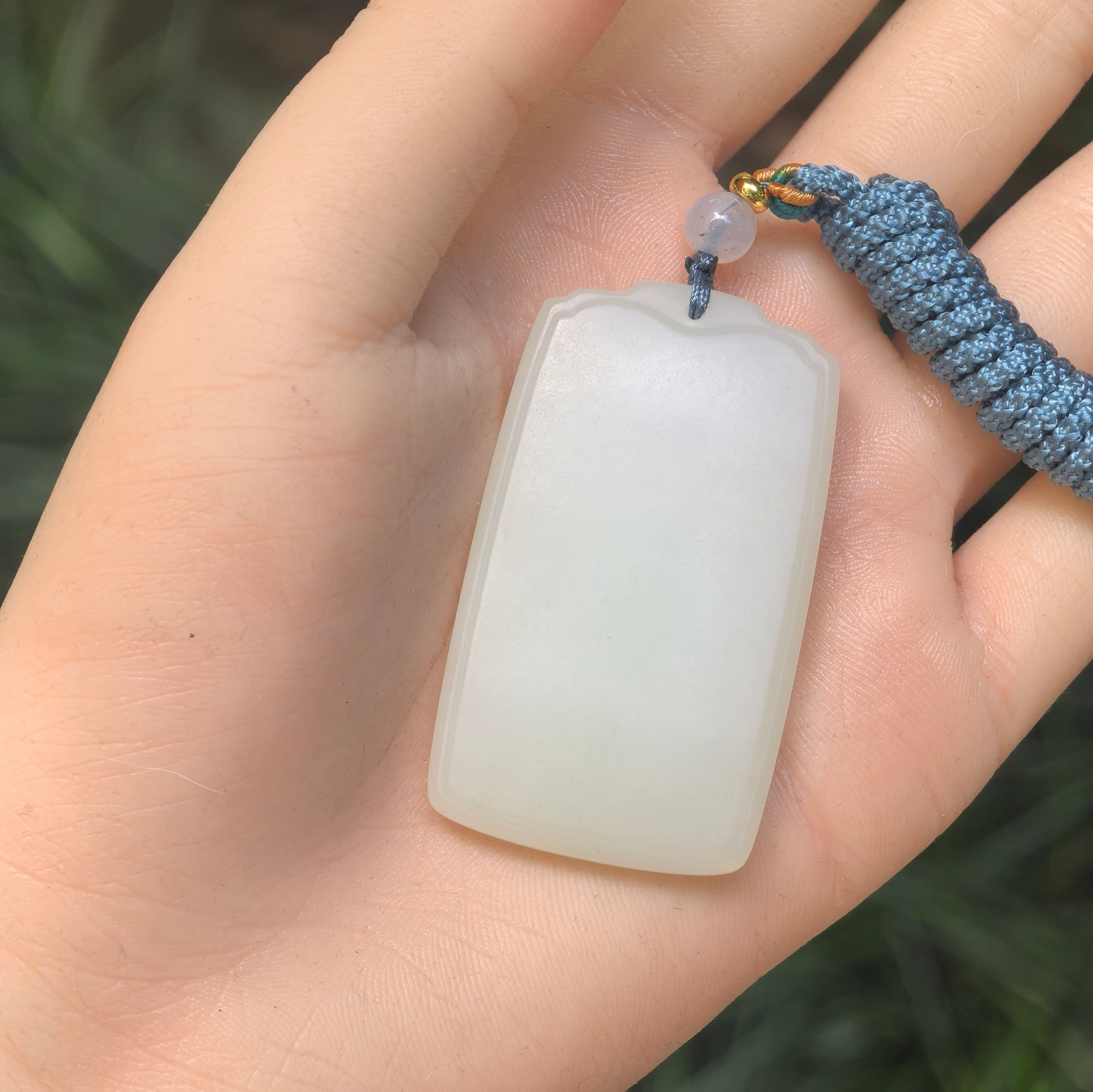Blue-white Hetian jade plain plaque pendant shown in hand with soft oily luster.
