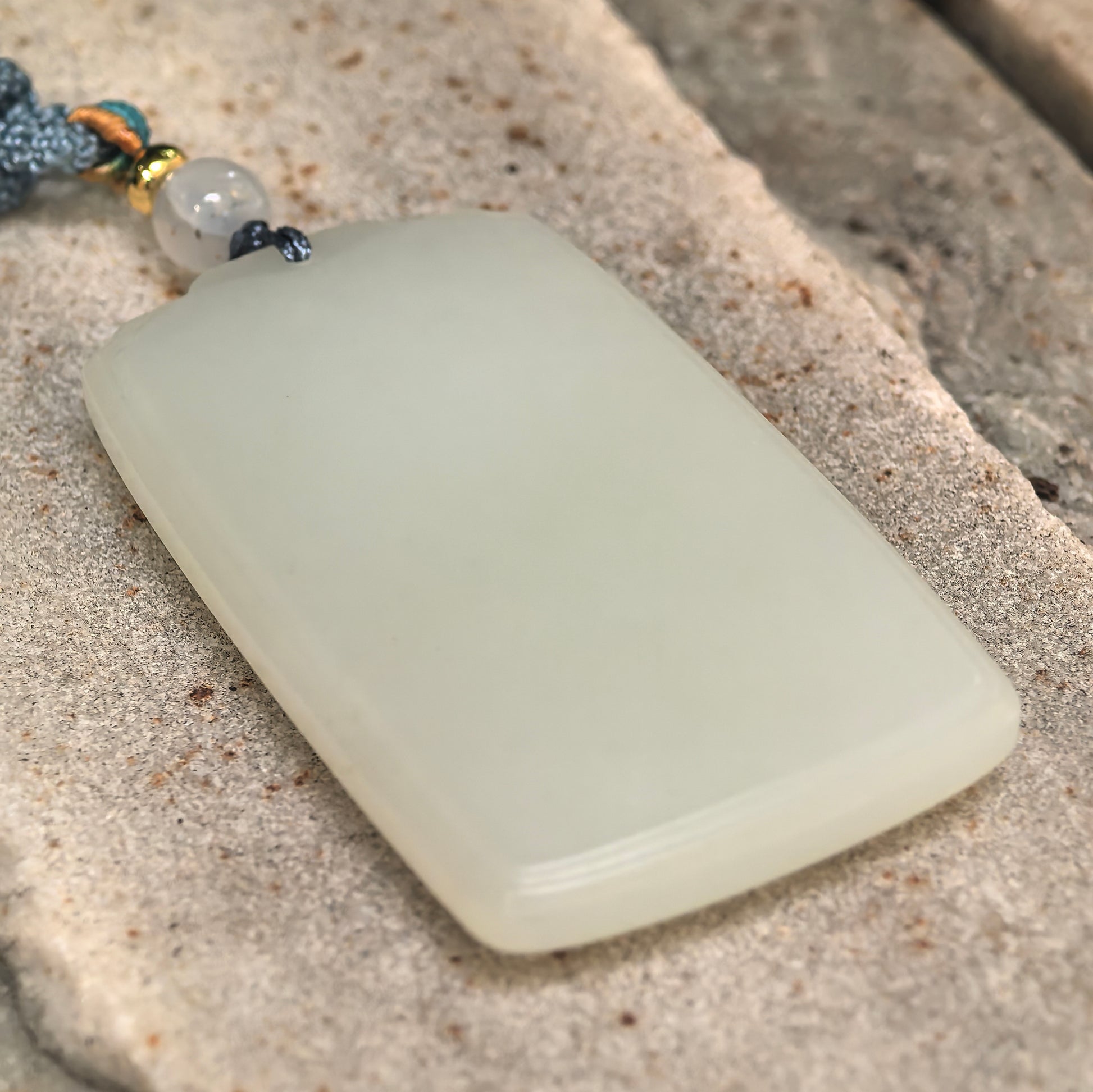 Side view of blue-white Hetian jade pendant showing polished edge and thickness.
