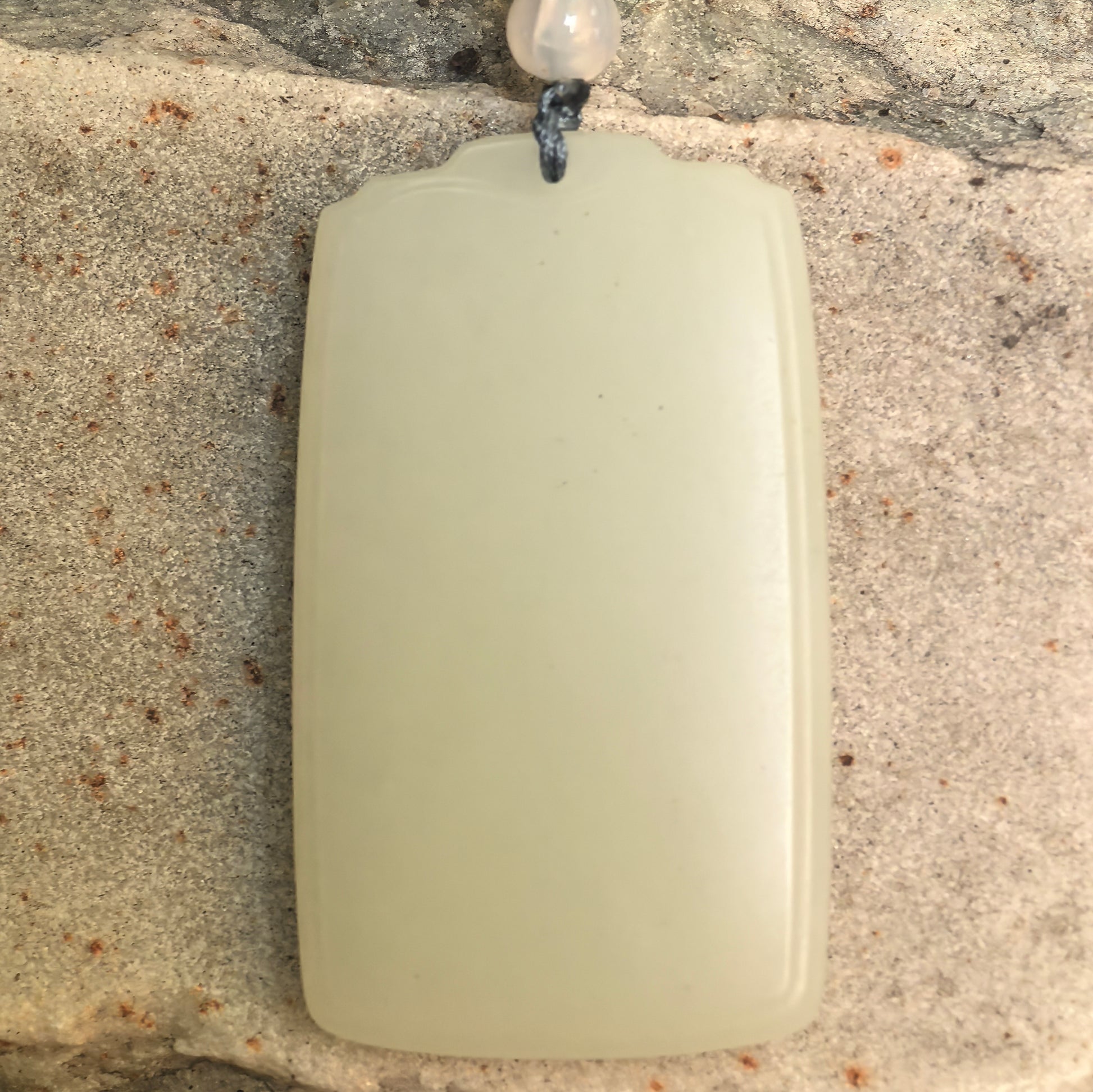 Close-up of natural Hetian jade plaque pendant showing smooth surface and clean rectangular form.
