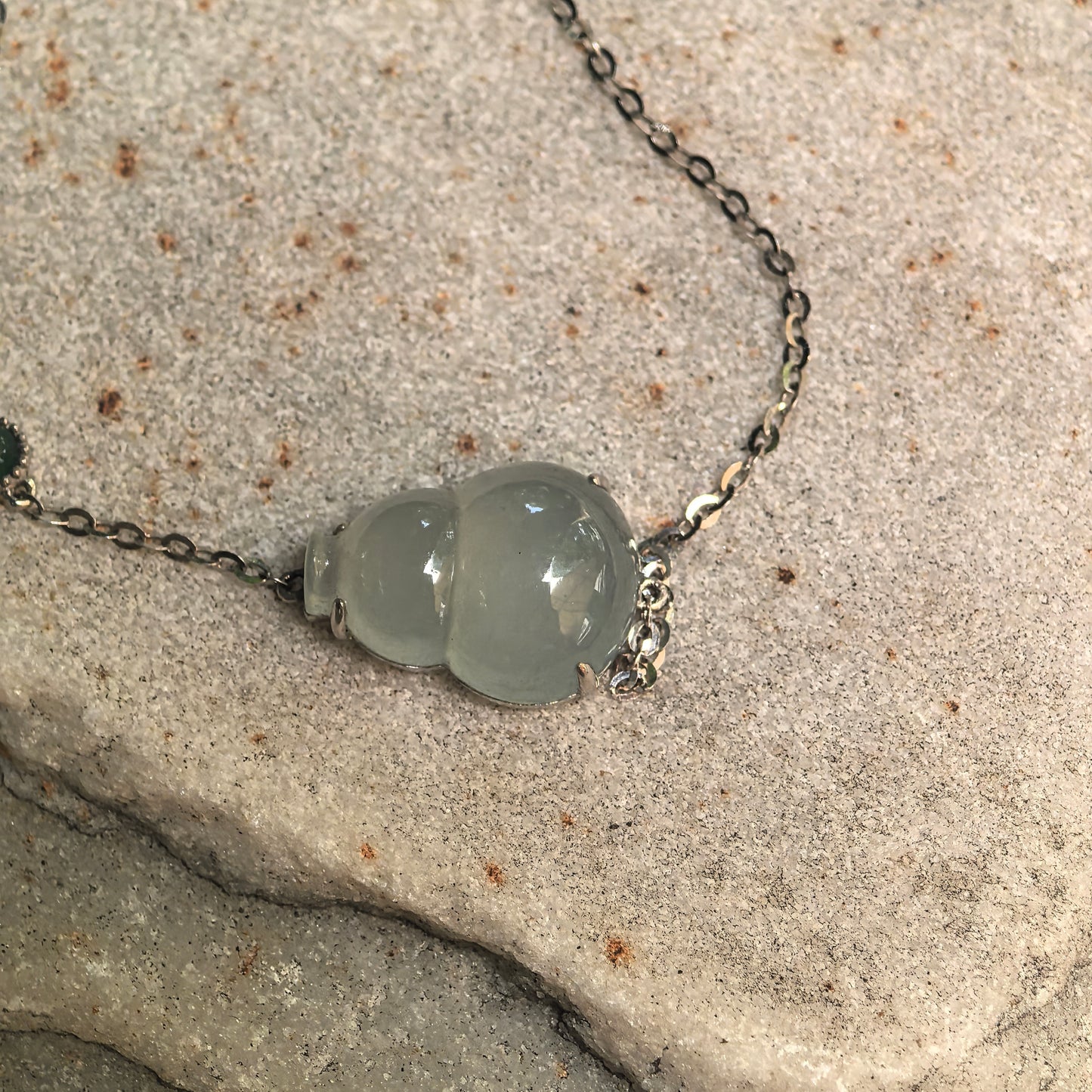Natural Grade-A jadeite gourd bracelet with fine 18K gold chain shown on stone background.
