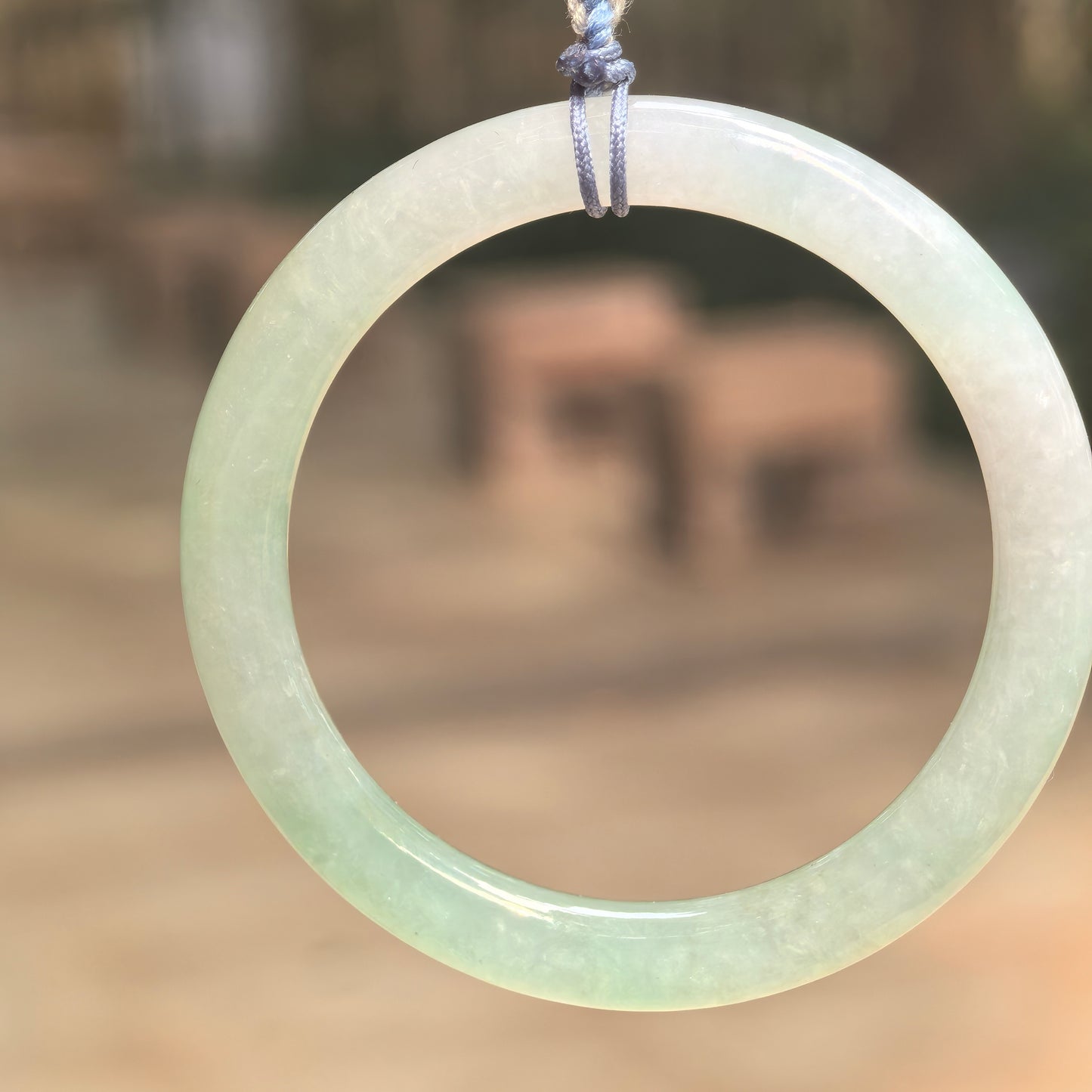 Natural Grade-A icy glutinous light green child jadeite bangle hanging on cord with soft translucent luster.
