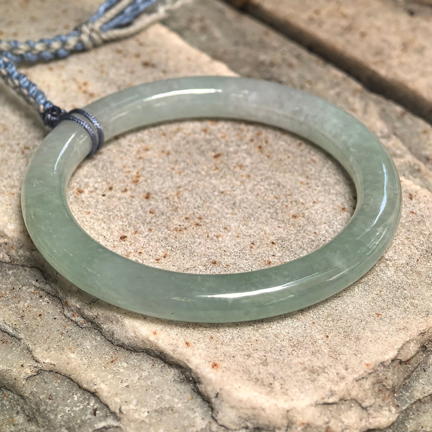 Close-up of icy glutinous light green jadeite bangle used as a pendant-style ornament.
