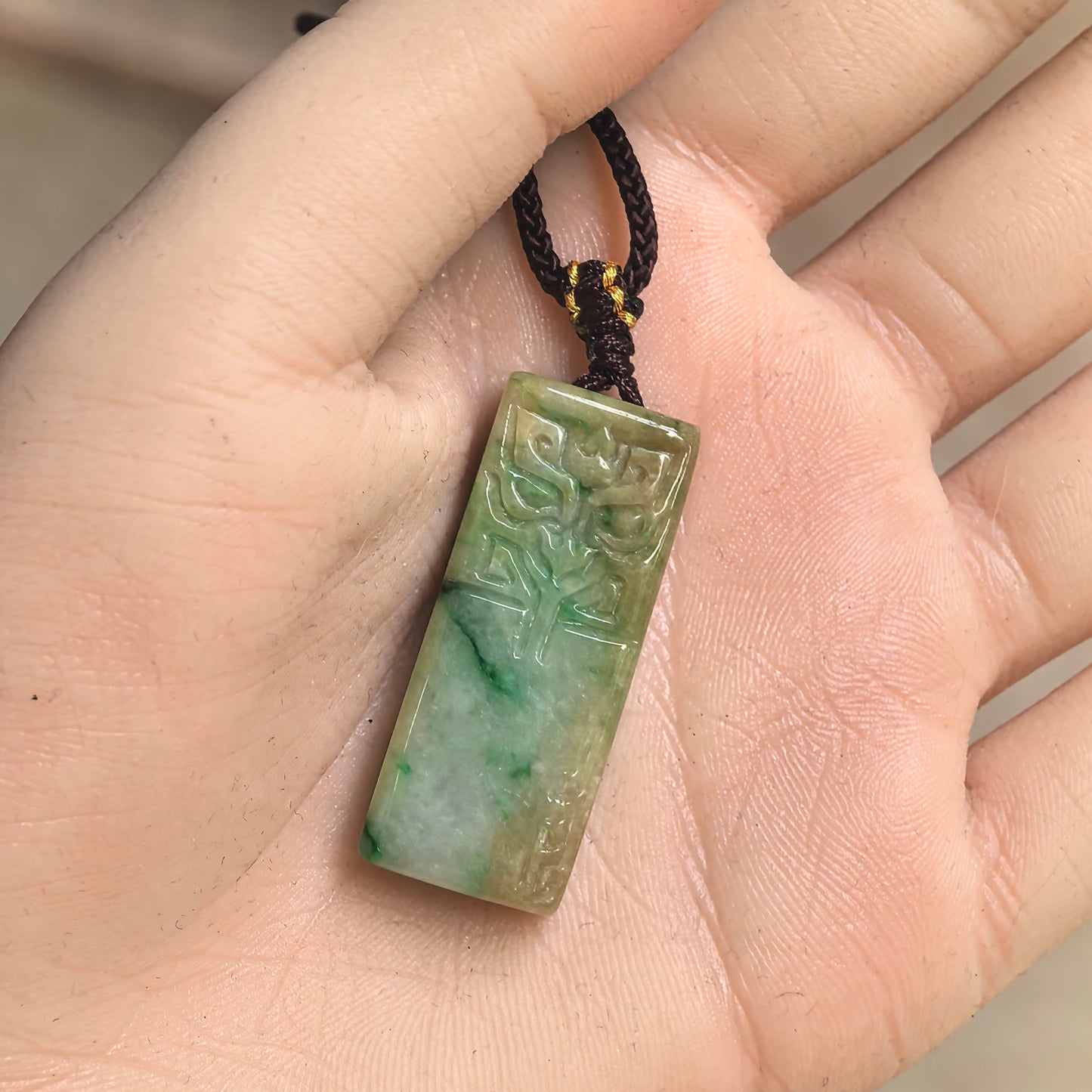 Glutinous yellow-green jadeite pendant shown in hand with rectangular plaque shape.
