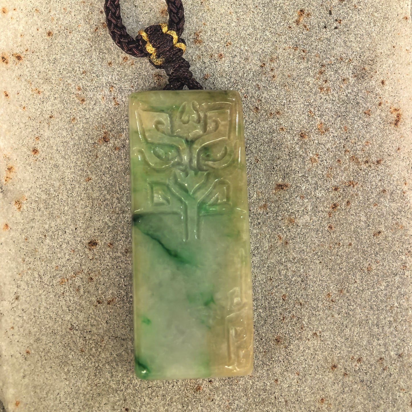 Close-up of carved archaic mask jadeite pendant with light green and brownish-yellow tones.
