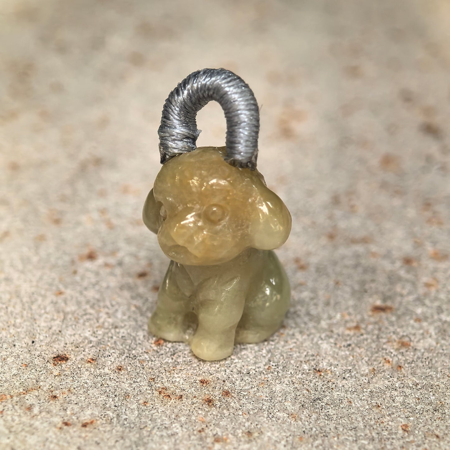 Close-up of small light yellow puppy jadeite charm showing rounded ears and glossy luster.
