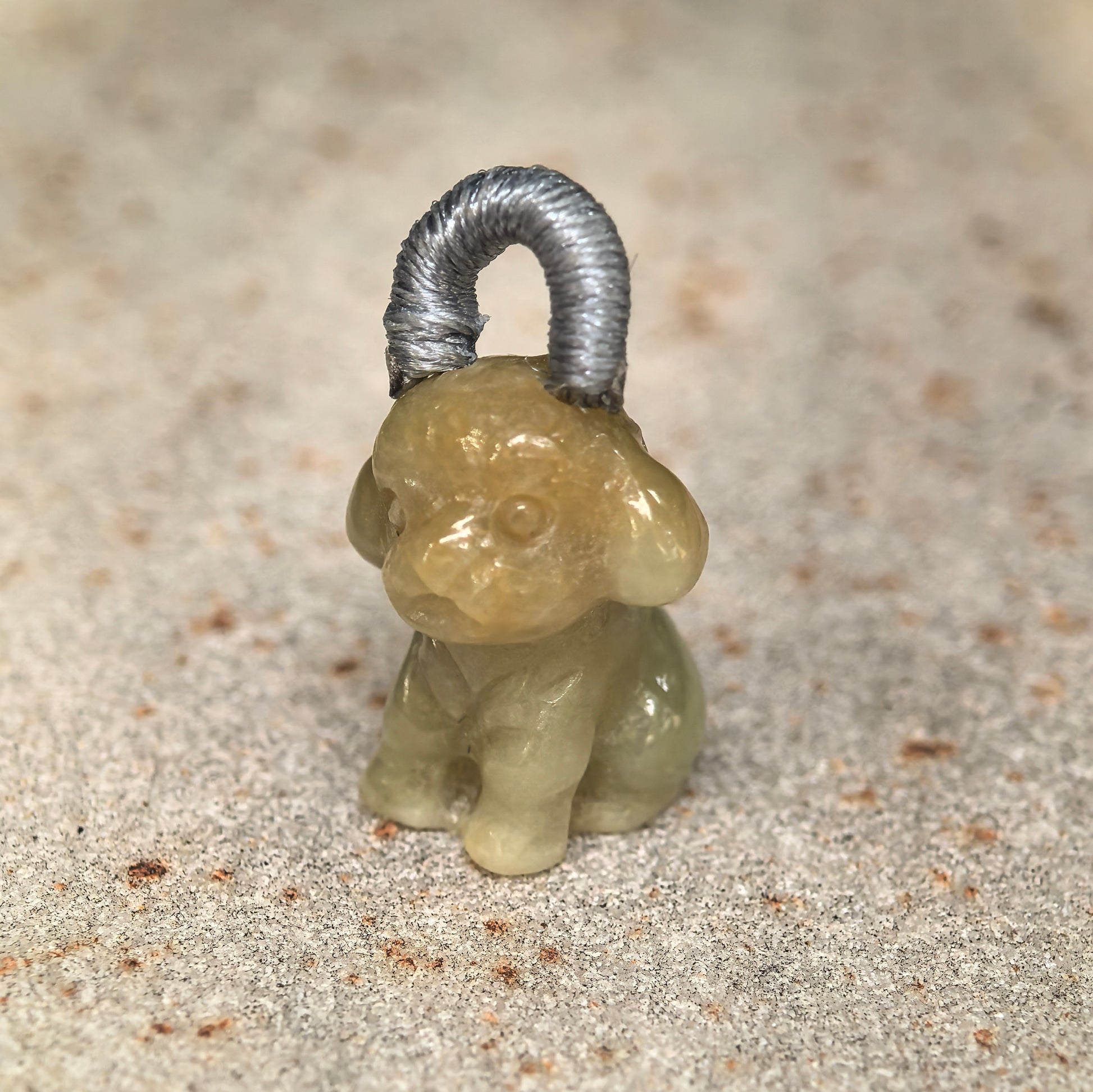 Close-up of small light yellow puppy jadeite charm showing rounded ears and glossy luster.
